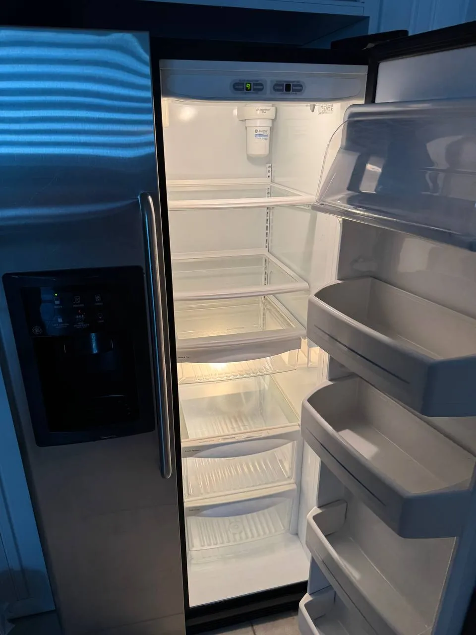 Kenmore side-by-side refrigerator standing open and empty with the water filter in the ceiling of the fresh-food section