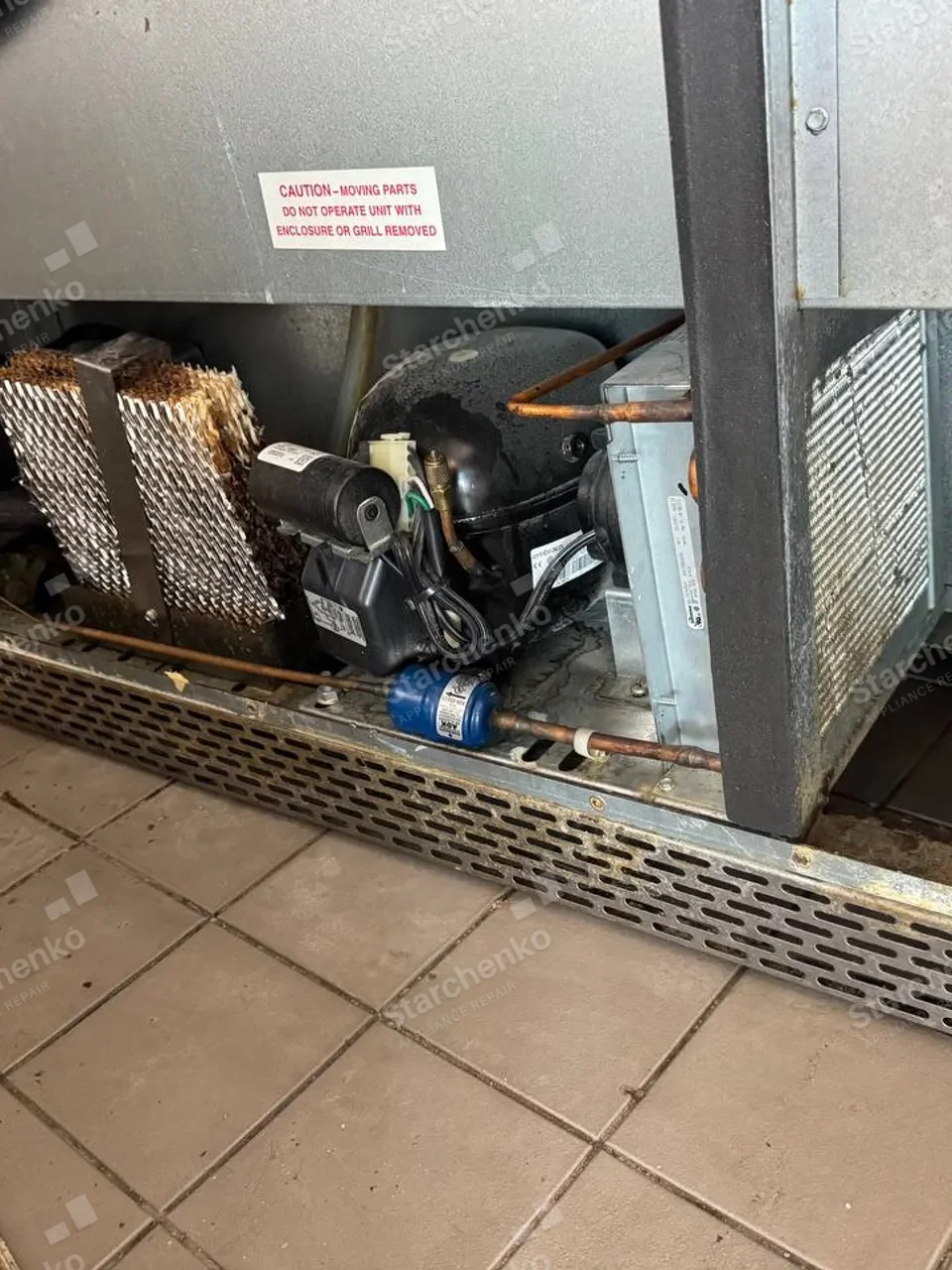 Commercial refrigerator compressor compartment with a clogged condenser coil and blue filter drier above a tile floor