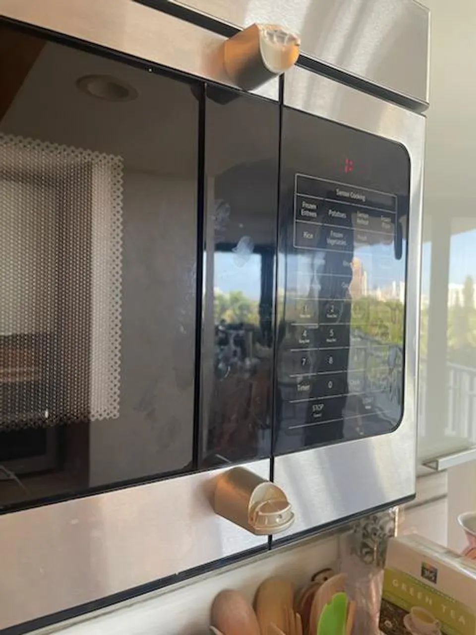 Close view of a stainless GE microwave with a black glass control panel and damaged handle