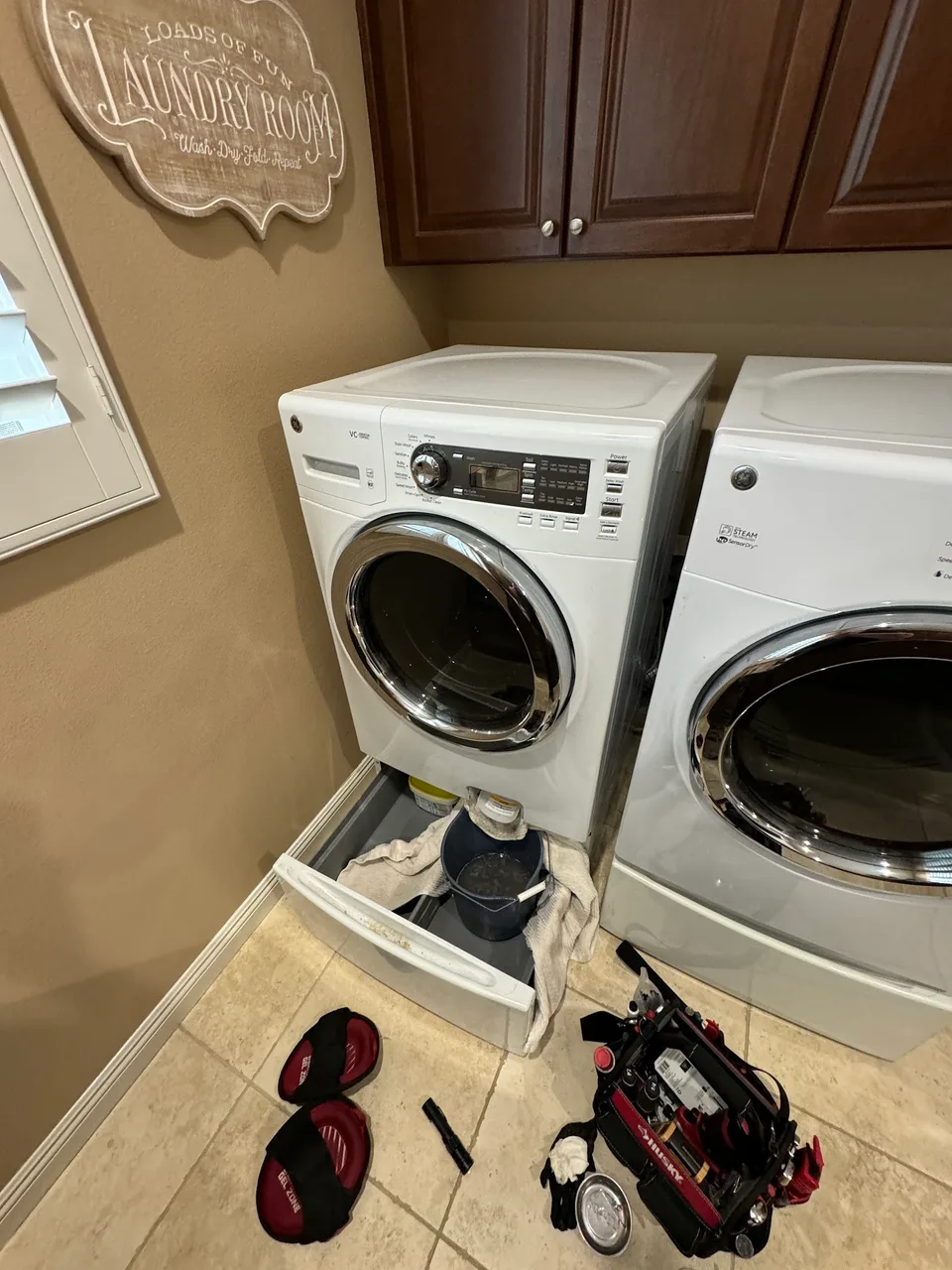 GE front-load washer with the pedestal drawer open and a bucket catching water