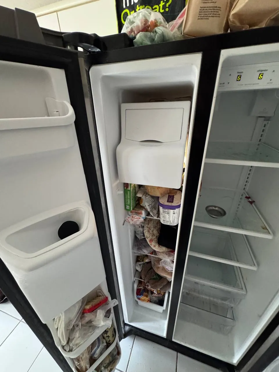 Open Whirlpool side-by-side refrigerator with a packed freezer and empty refrigerator shelves