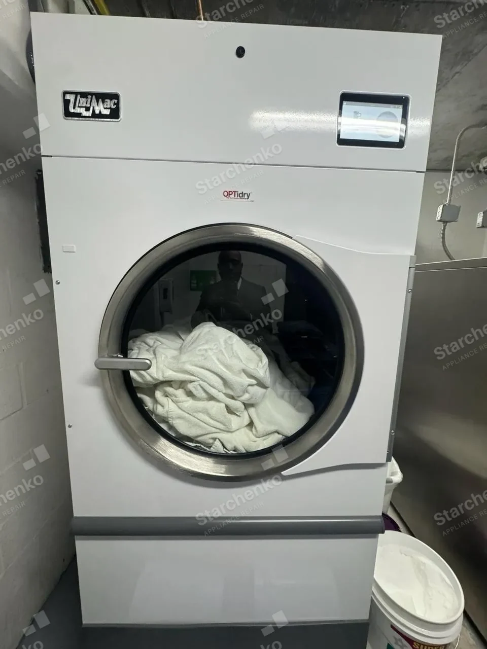 UniMac commercial dryer with white laundry in the drum and a touch panel above the door