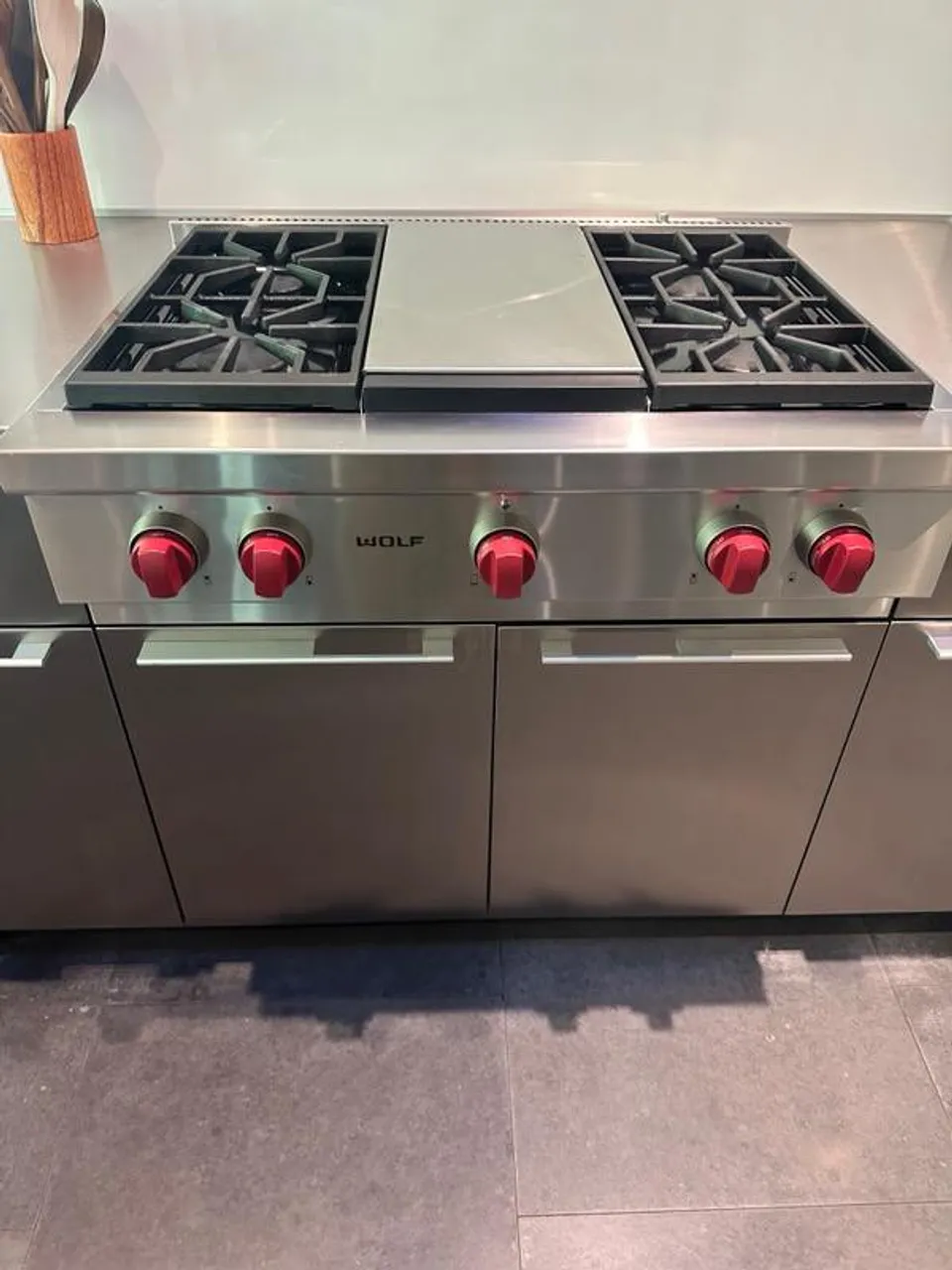 Stainless Wolf gas rangetop with red control knobs and a griddle plate between the two burner groups