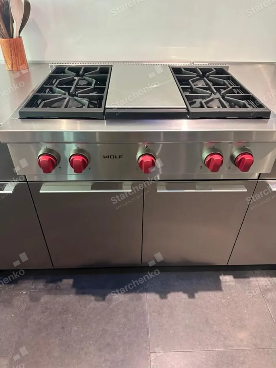 Stainless Wolf gas rangetop with red control knobs and a griddle plate between the two burner groups