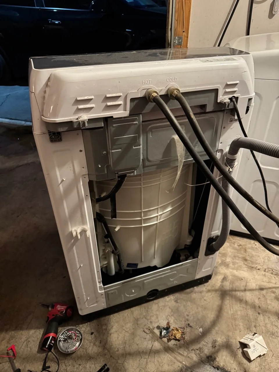 Top-load washer pulled out with its back panel removed and hoses still connected