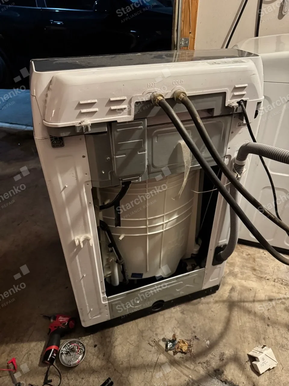 Whirlpool top-load washer pulled out with its back panel removed and hoses still connected