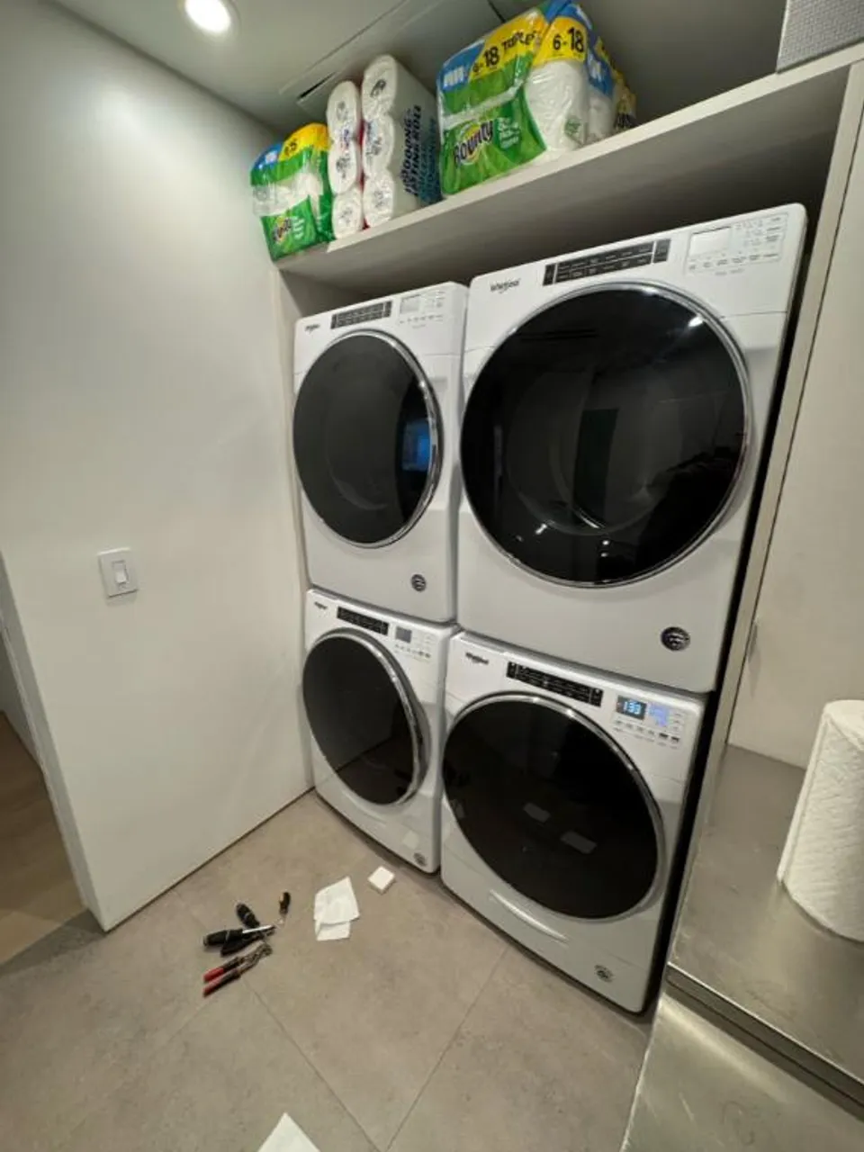 Two Whirlpool washer and dryer pairs stacked side by side with tools on the floor