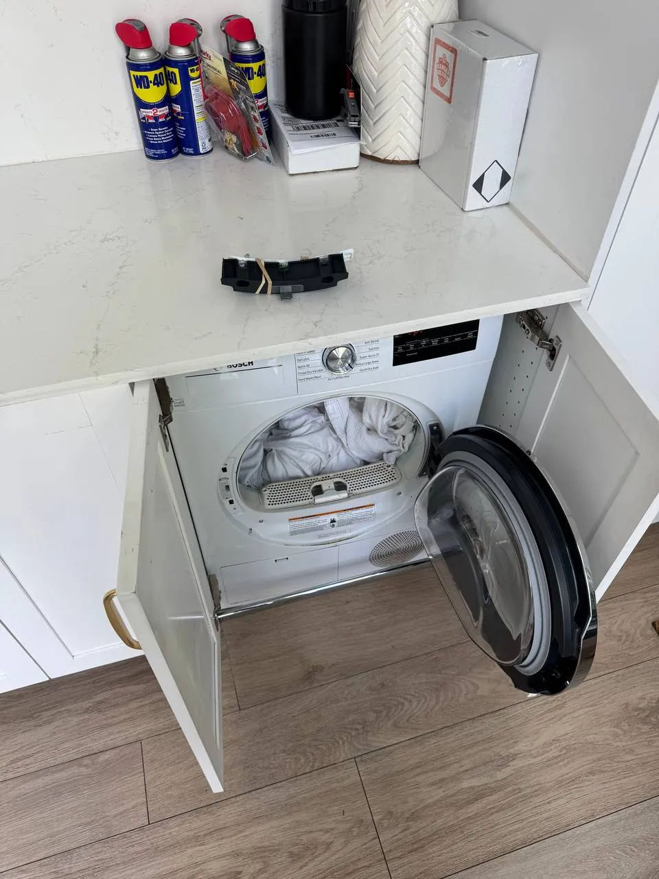 Bosch dryer under a counter with the door open and a drain component on the countertop