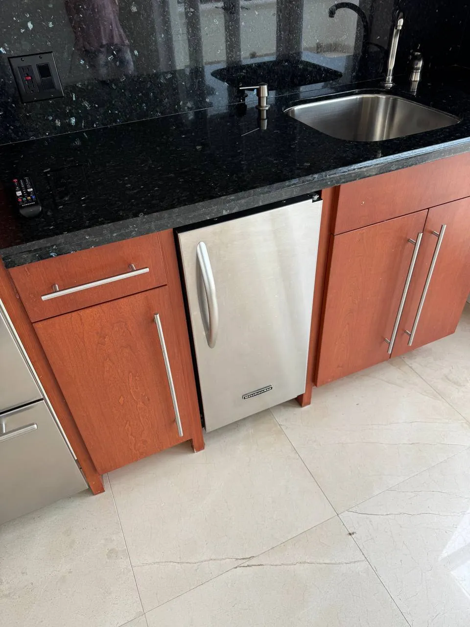 Stainless KitchenAid undercounter ice maker below a black stone countertop