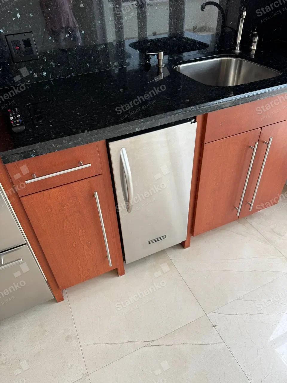 Stainless KitchenAid undercounter ice maker below a black stone countertop