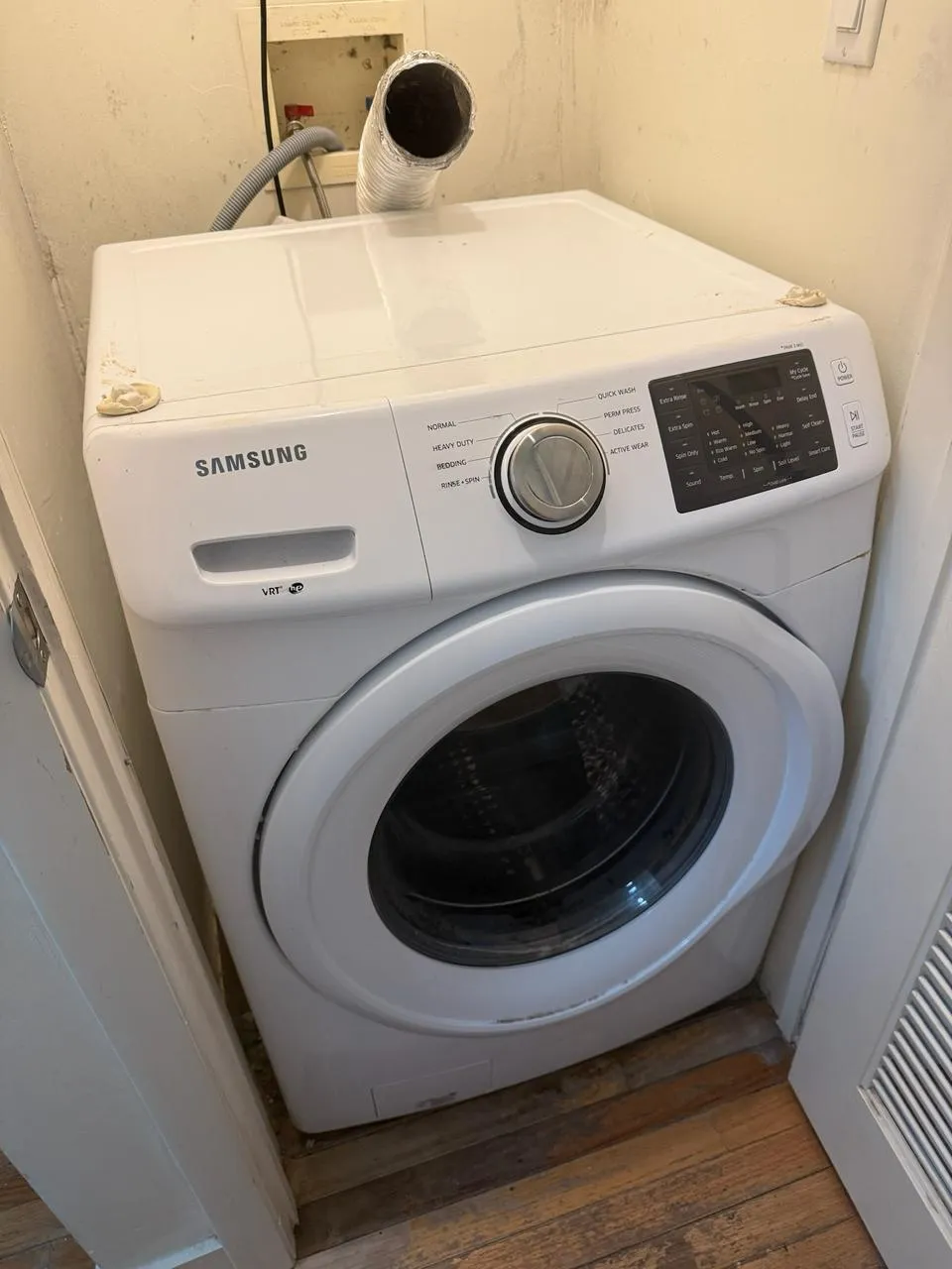 Samsung front-load washer in a narrow laundry closet with the vent duct above it