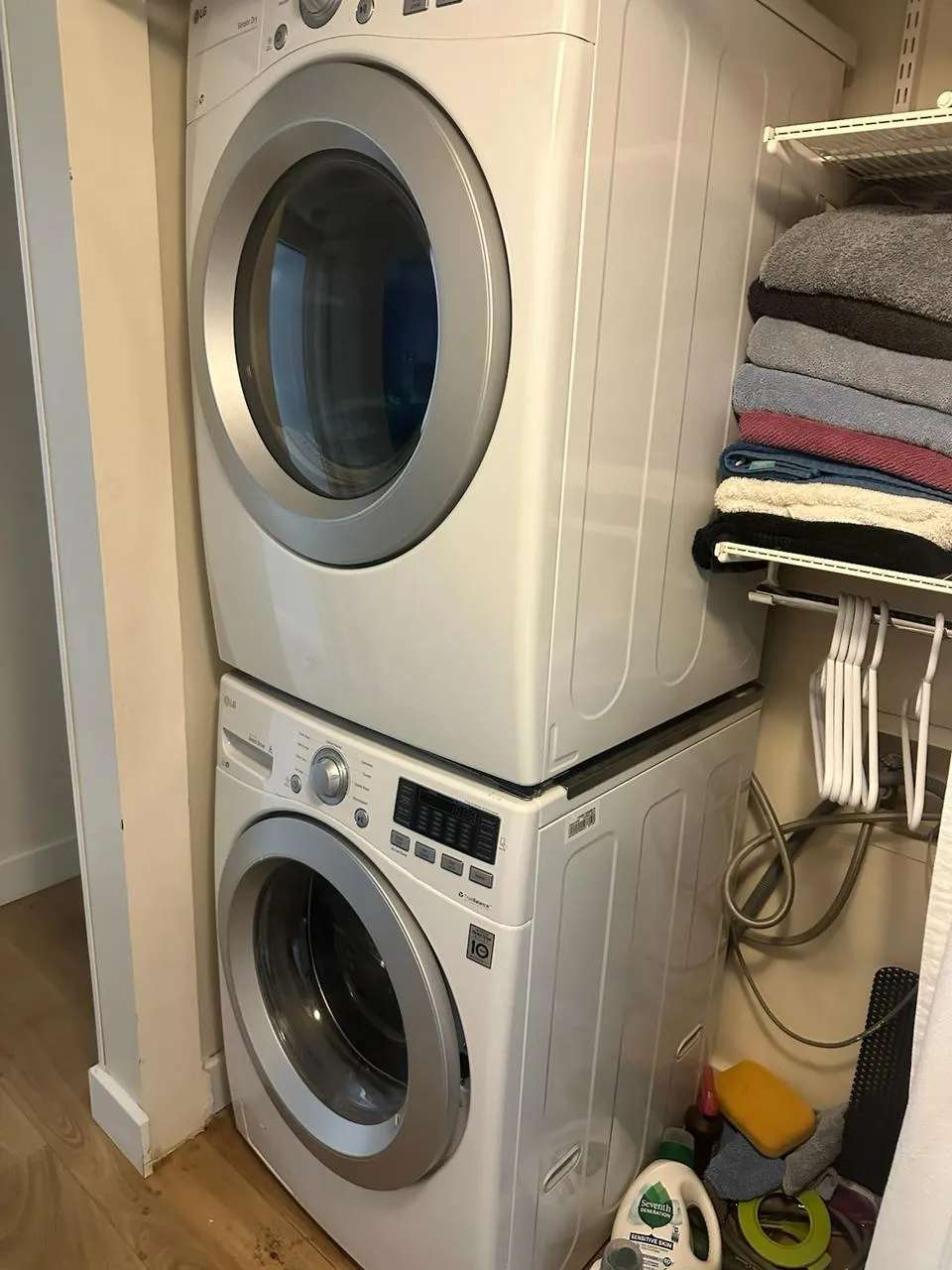 LG washer and dryer stacked in a home laundry niche beside a shelf of towels