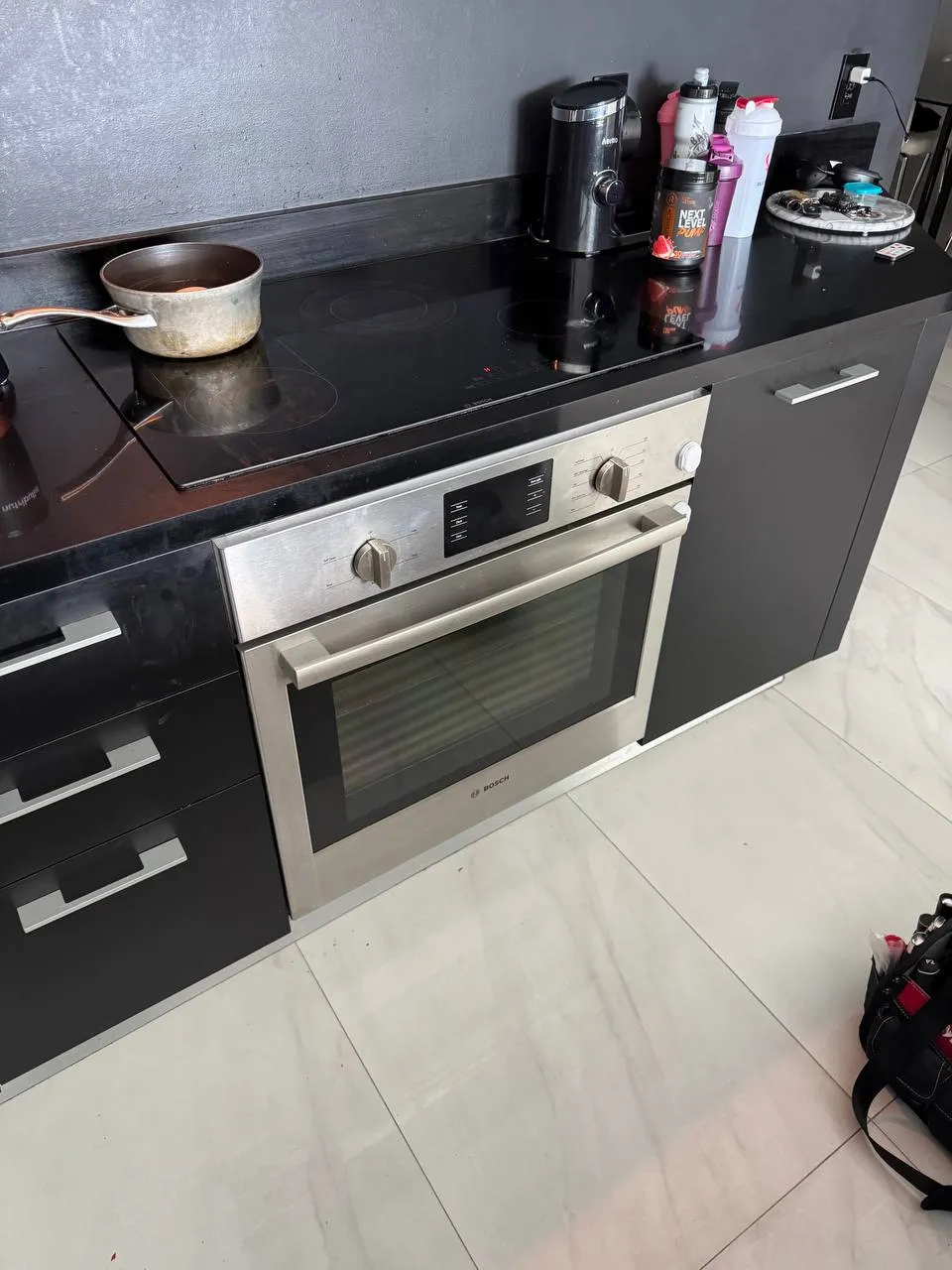 Bosch wall oven below a black glass cooktop with pots and bottles on the counter