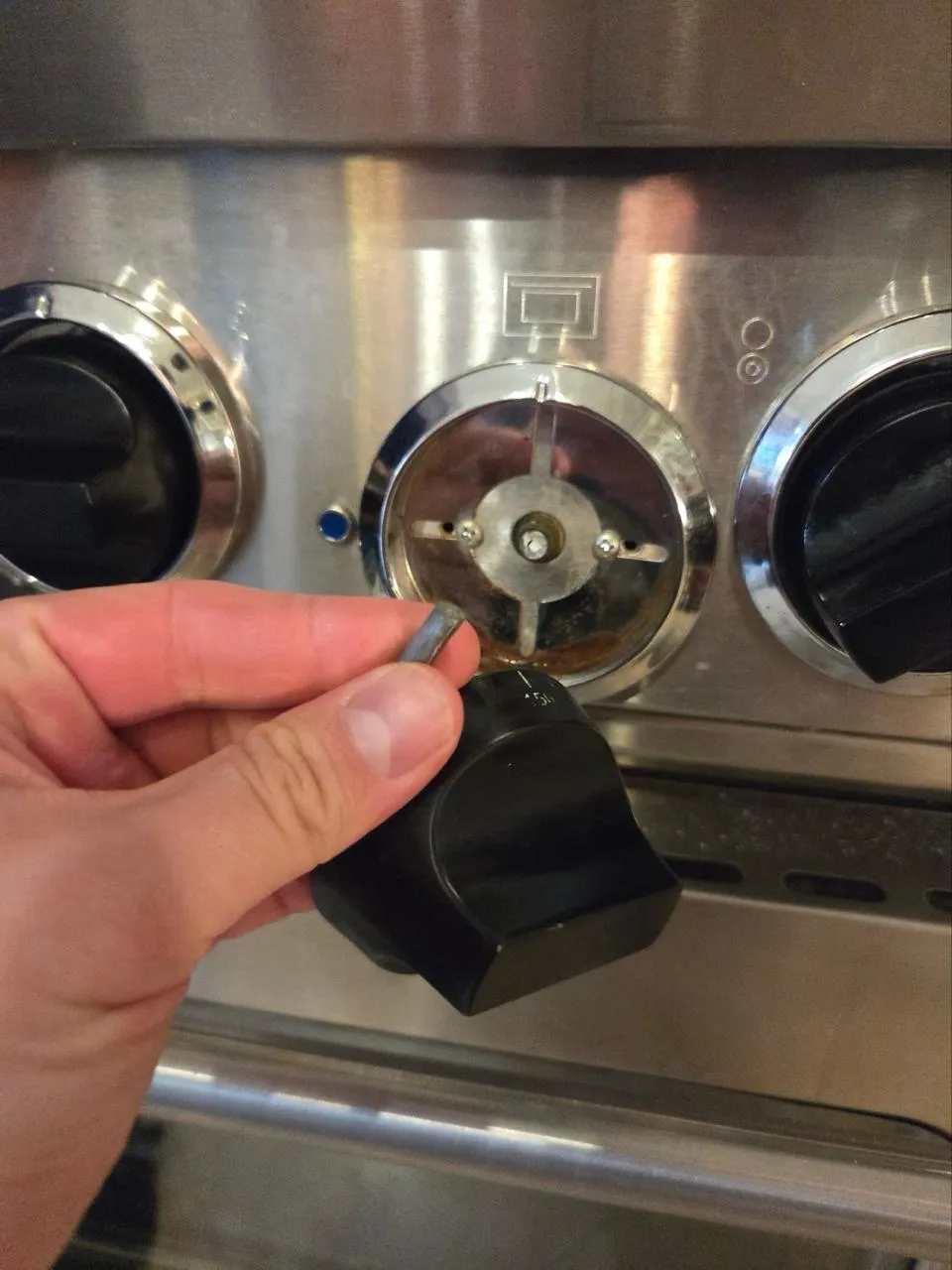 Close-up of a hand pulling the control knob off the stainless panel of a Wolf range