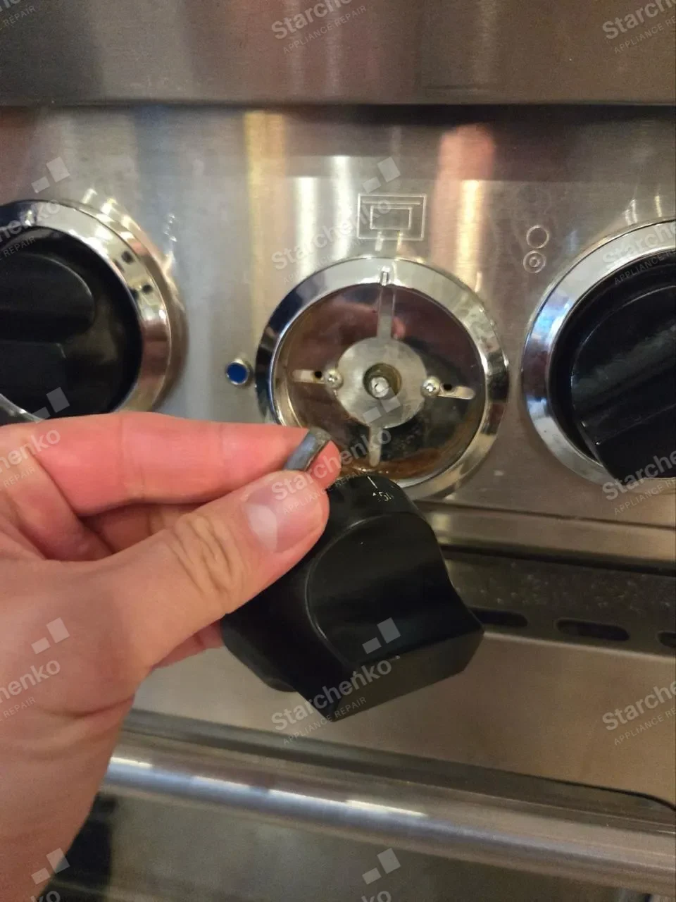 Close-up of a hand pulling the control knob off the stainless panel of a Wolf range