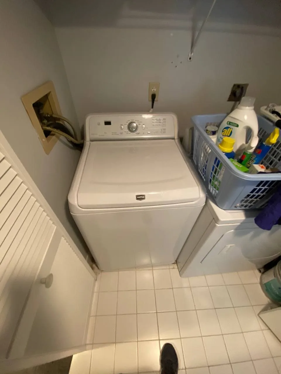 Top-load washer in a laundry room beside a basket of supplies