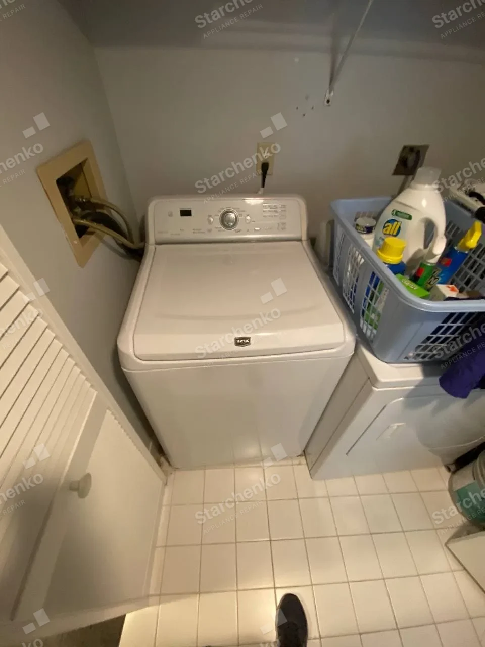 Maytag top-load washer in a laundry room beside a basket of supplies