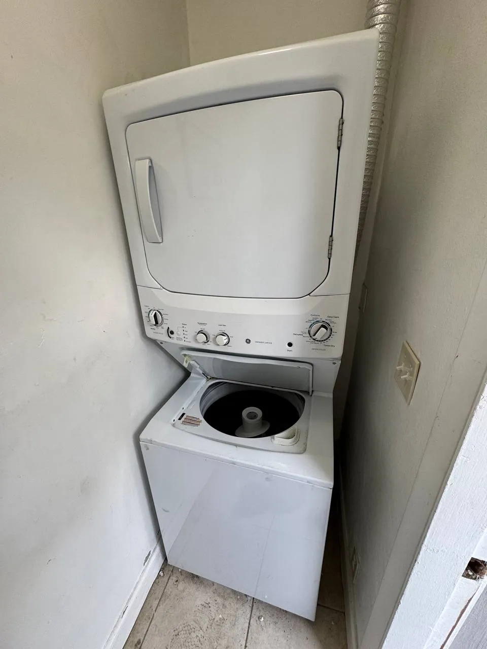 White GE stacked laundry center with the washer lid open in a narrow closet