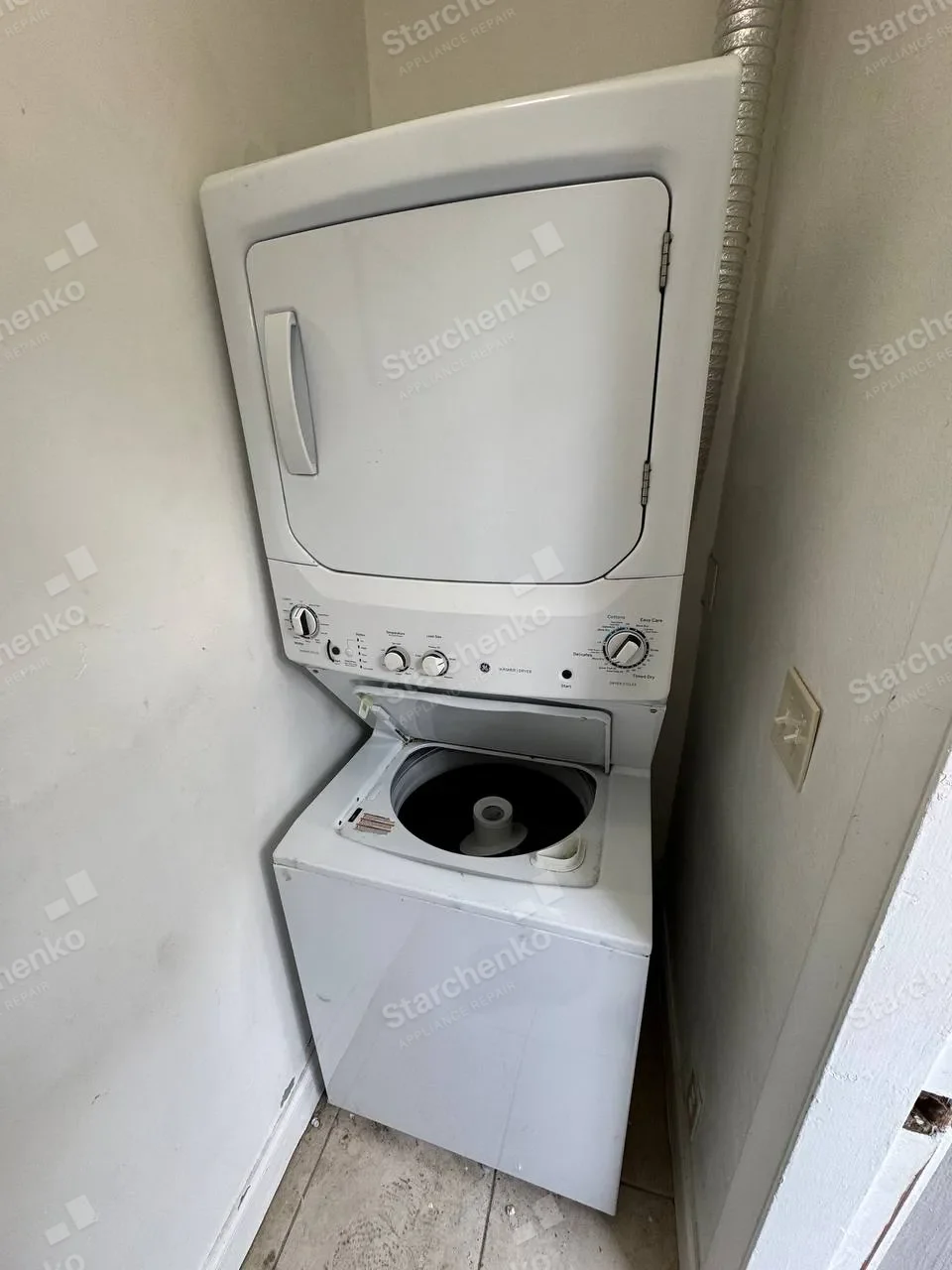 White GE stacked laundry center with the washer lid open in a narrow closet