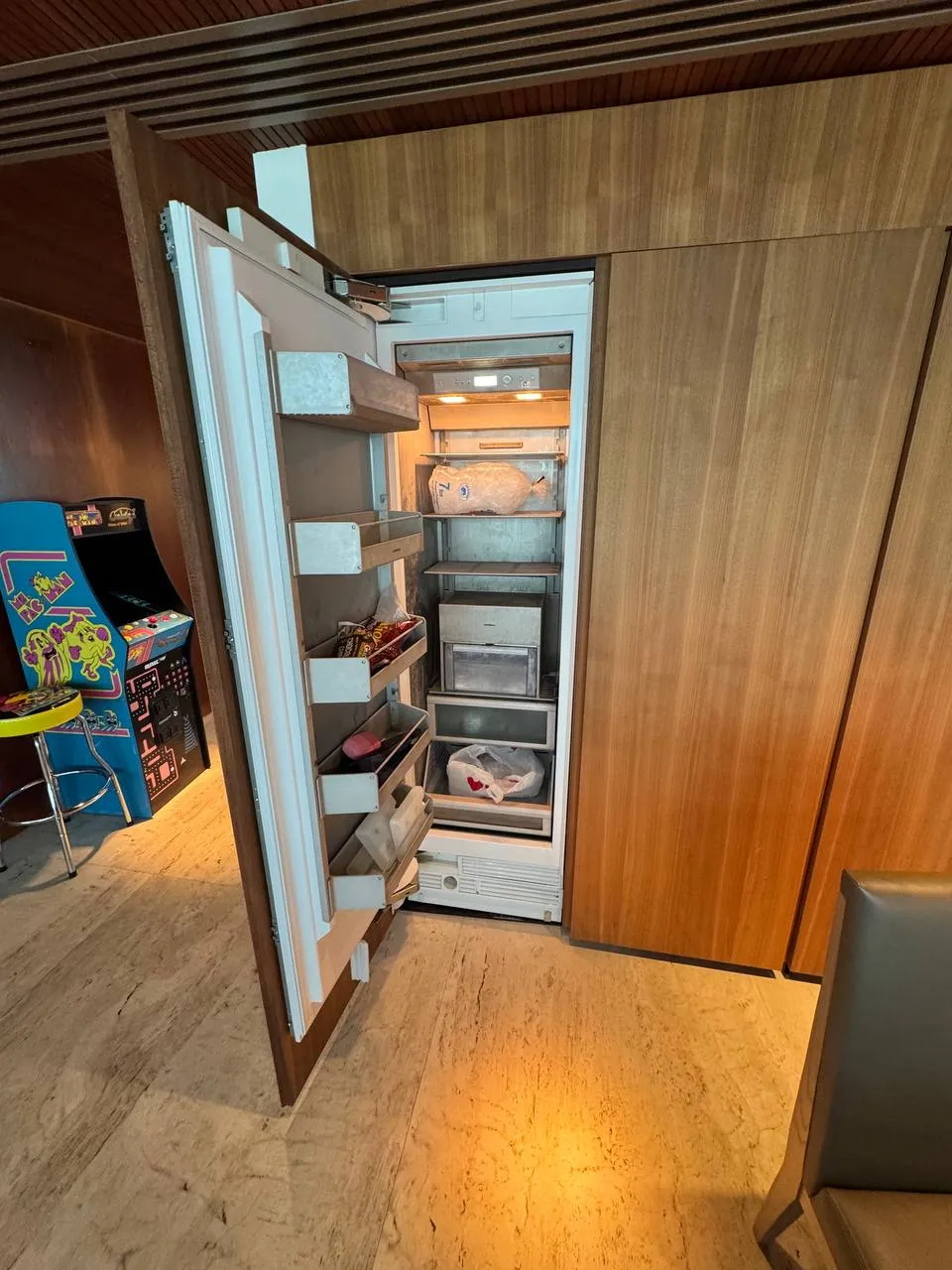 Built-in Miele refrigerator column with its panel-ready door swung open in a wood-paneled room
