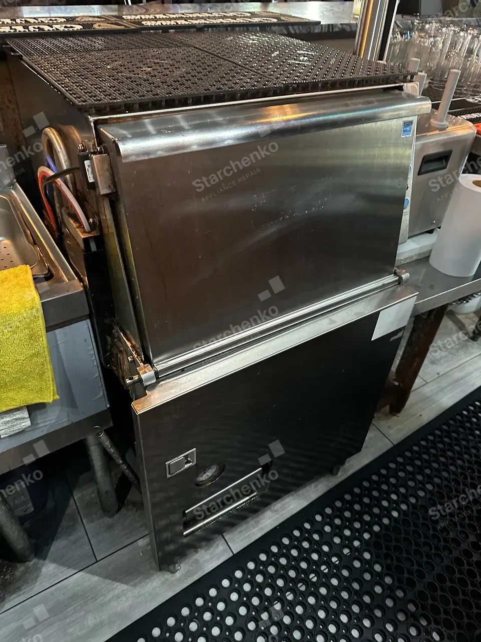 Stainless under-counter commercial dishwasher in a bar service area with its door closed