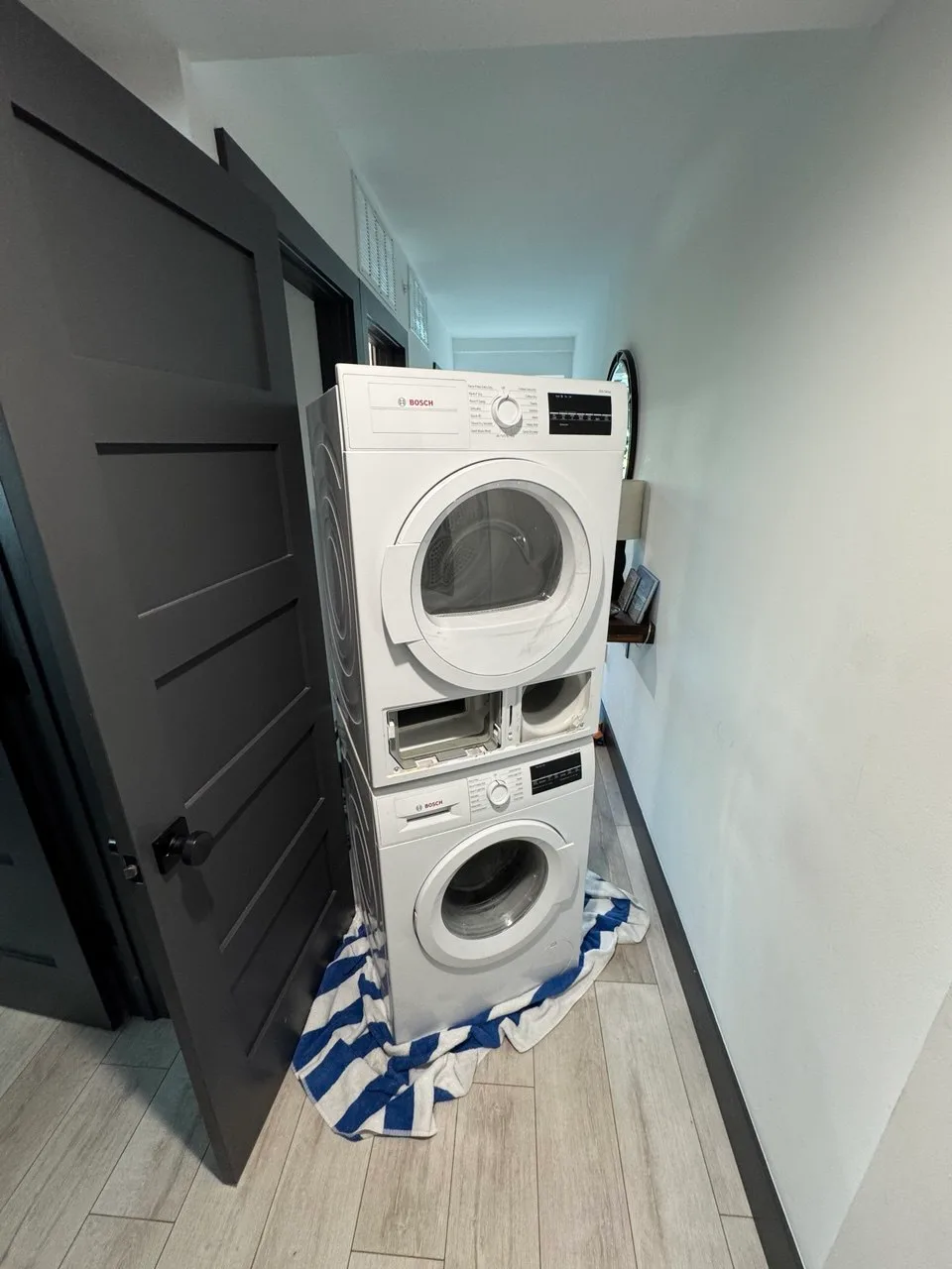 Compact Bosch washer-dryer stack in a hallway with a towel under the washer