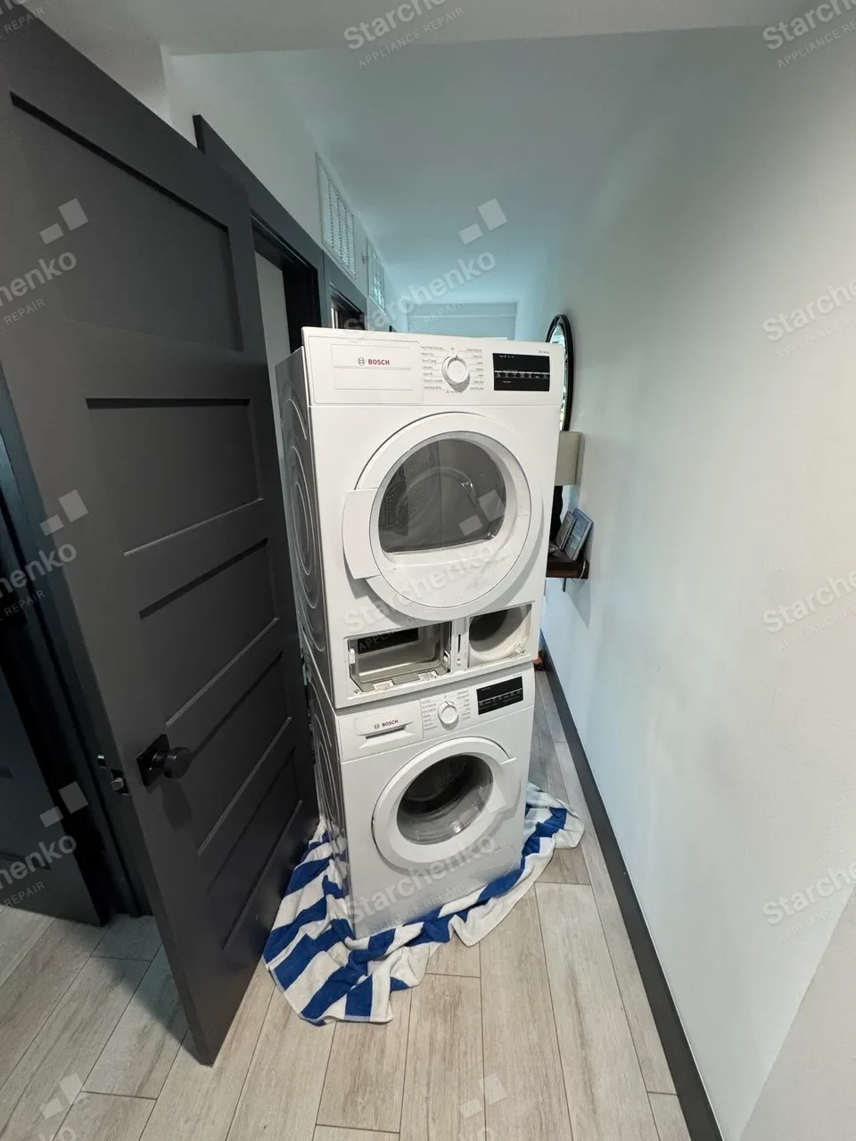 Bosch compact washer-dryer stack in a hallway with a towel under the washer