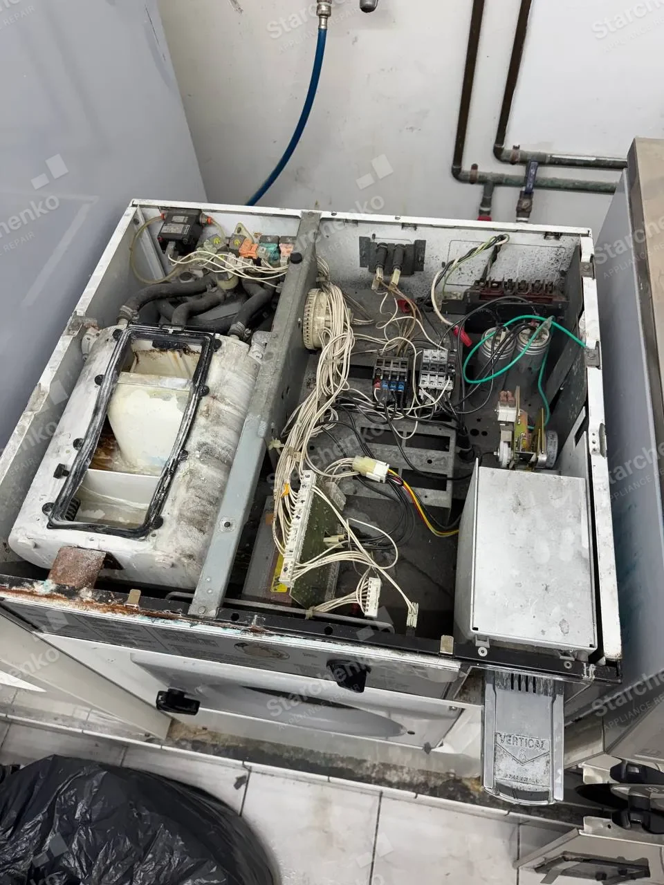 Commercial washer opened from the top with wiring and controls exposed