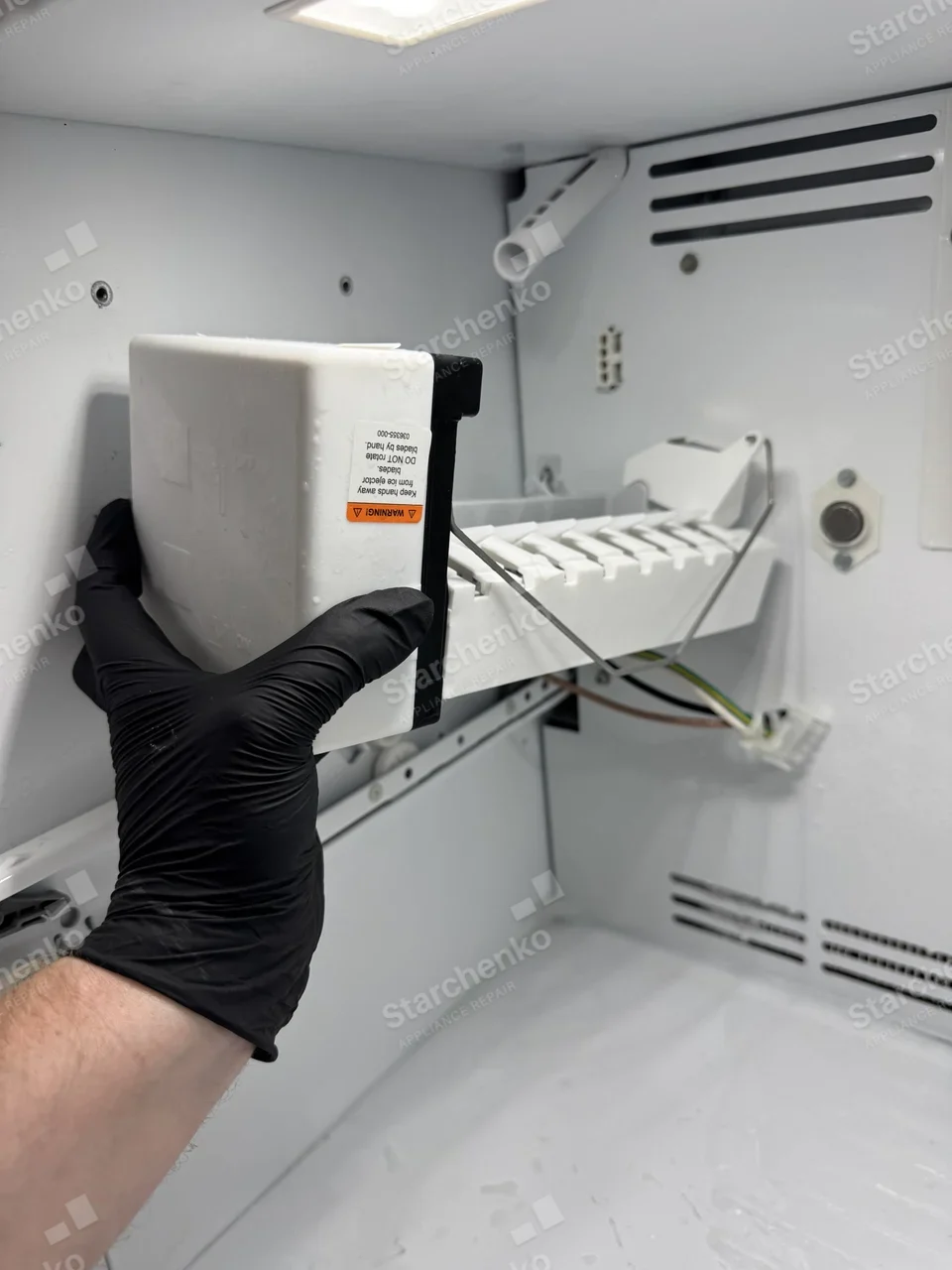 Technician holding a Frigidaire refrigerator ice maker assembly in front of its freezer mount