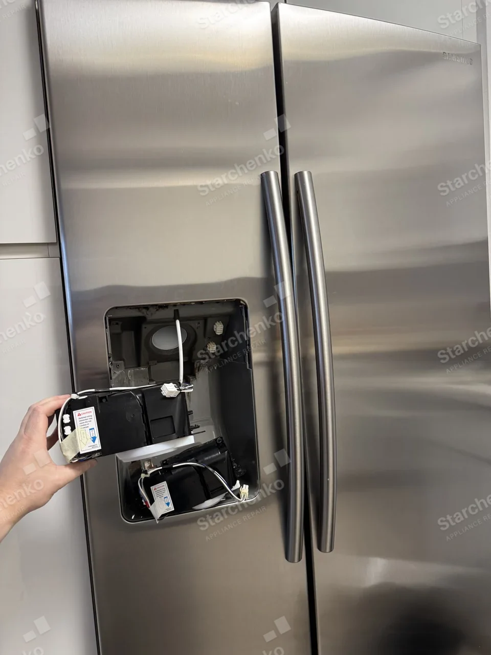 Samsung side-by-side refrigerator with the dispenser housing removed and the old module held out