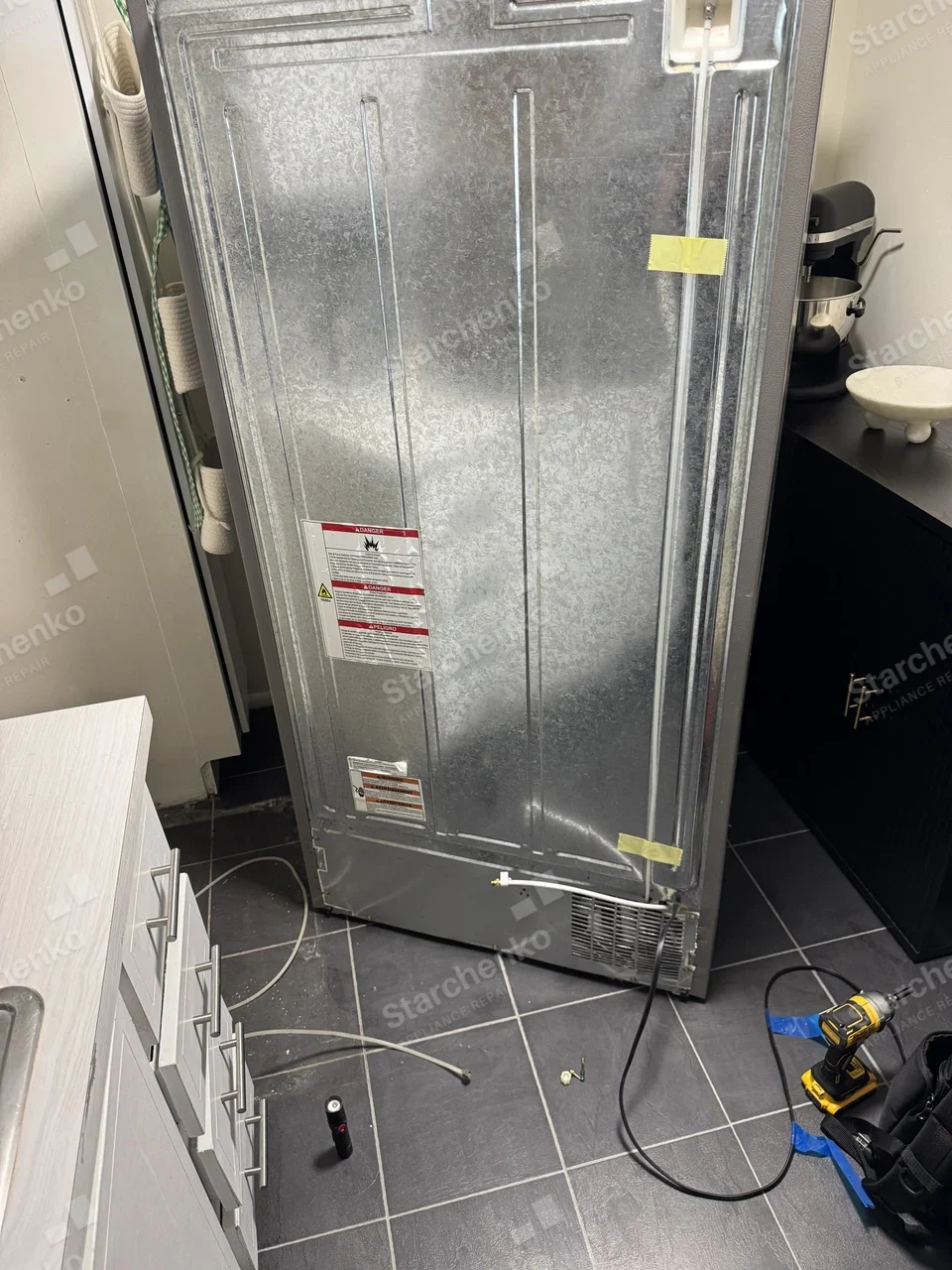 Back of an Amana refrigerator pulled away from the wall with its water line disconnected