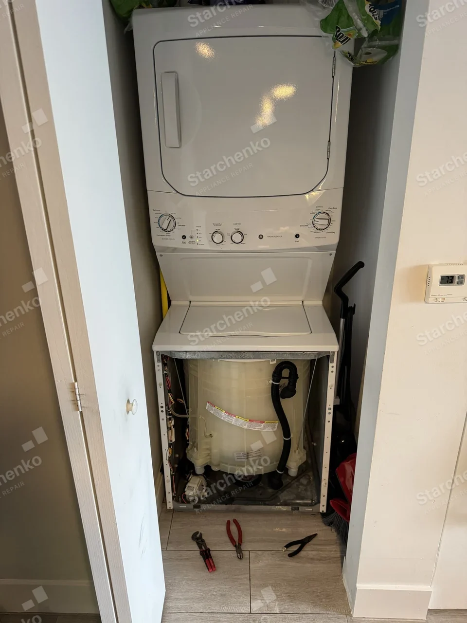 GE stacked washer and dryer in a closet with the washer front panel removed and pliers on the floor