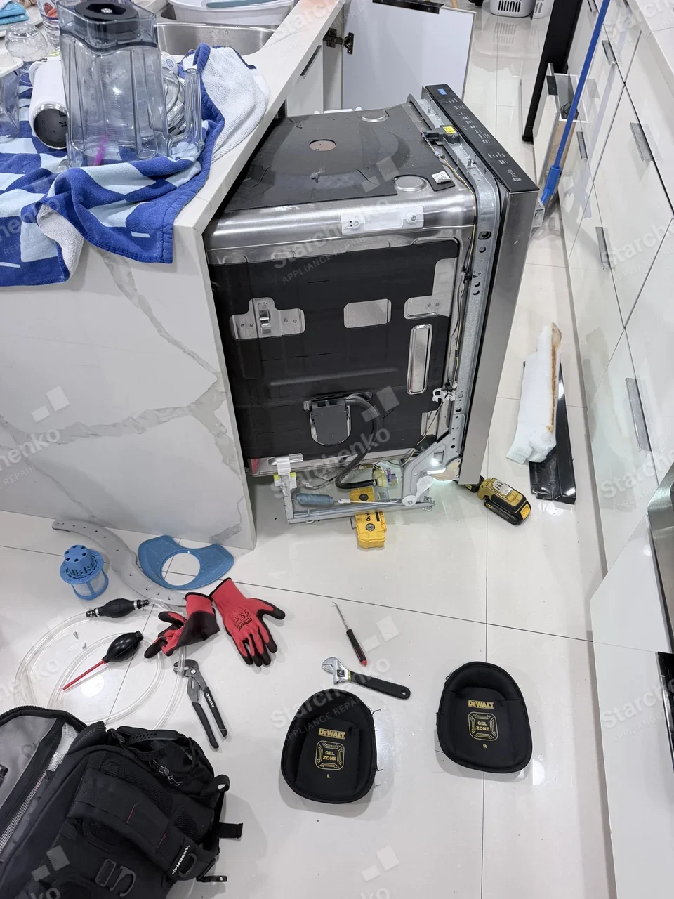 GE Profile dishwasher pulled out of the cabinet with parts and tools laid out on the floor