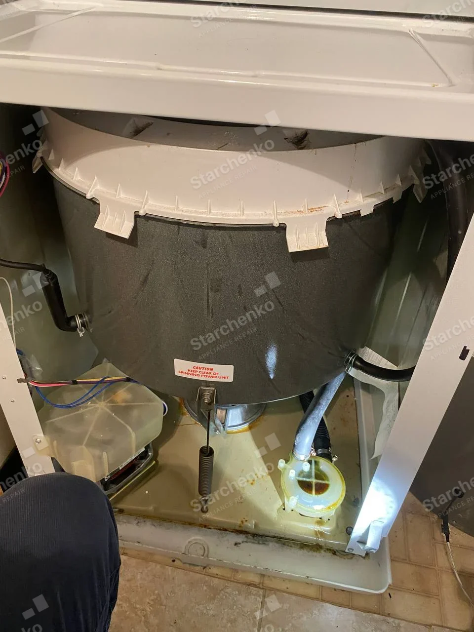 Samsung repair: Exposed outer tub, suspension spring and drain pump inside a top-load washer with front panel removed.