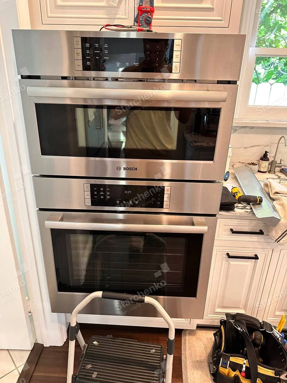 Bosch repair: Built-in upper microwave and lower oven with tester on top and trim removed from side.