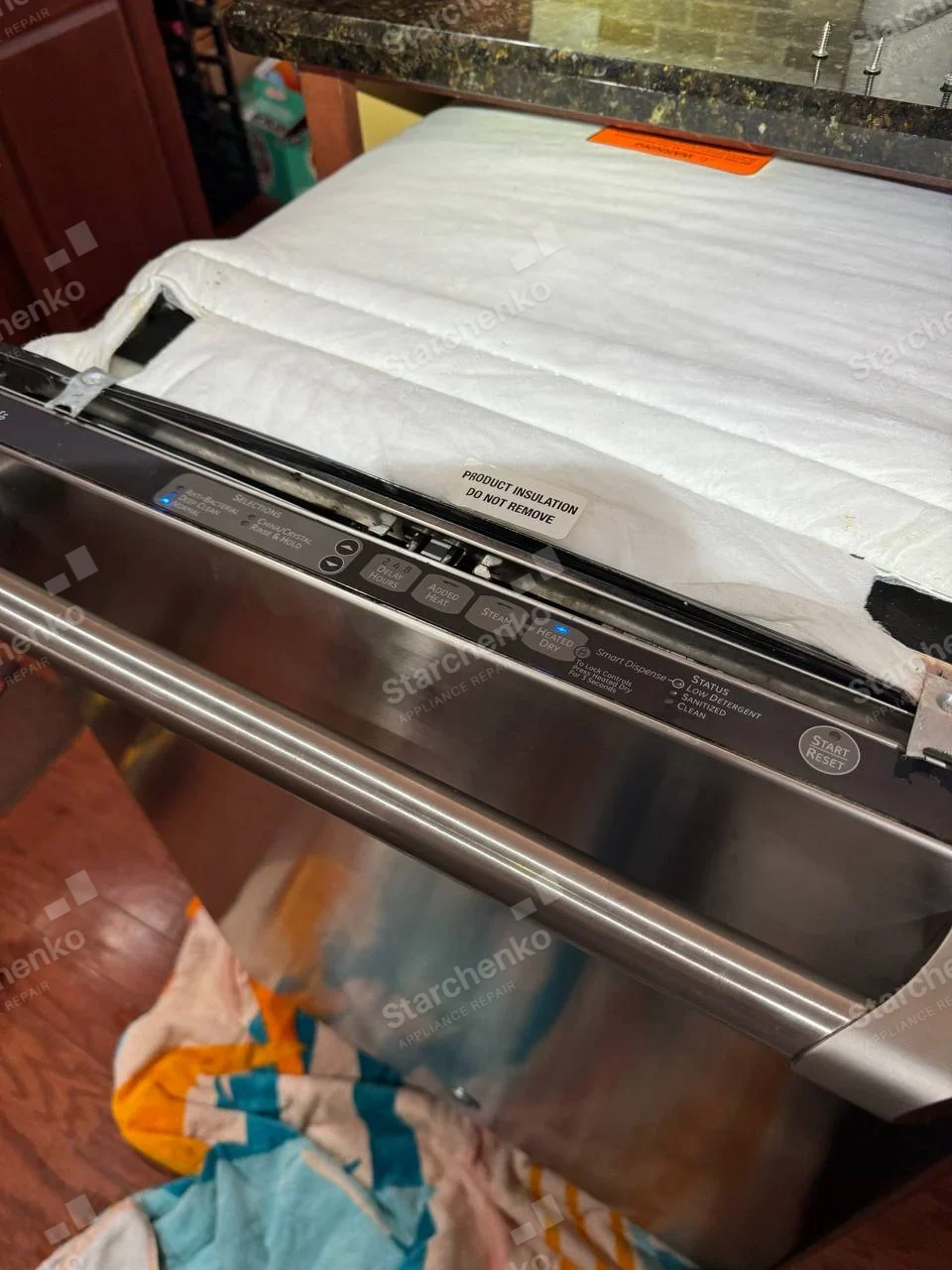 Samsung repair: Stainless dishwasher pulled forward, top insulation lifted and top-edge controls visible.