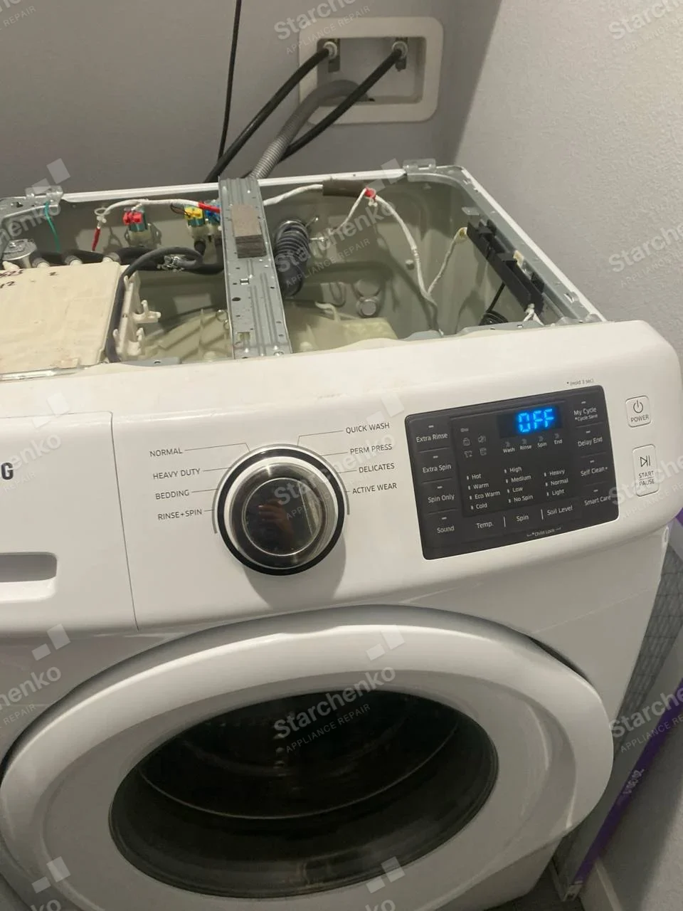 Kenmore repair: Front-load washer top panel removed, water hoses and valves exposed, brand lettering cut off at left edge of image.