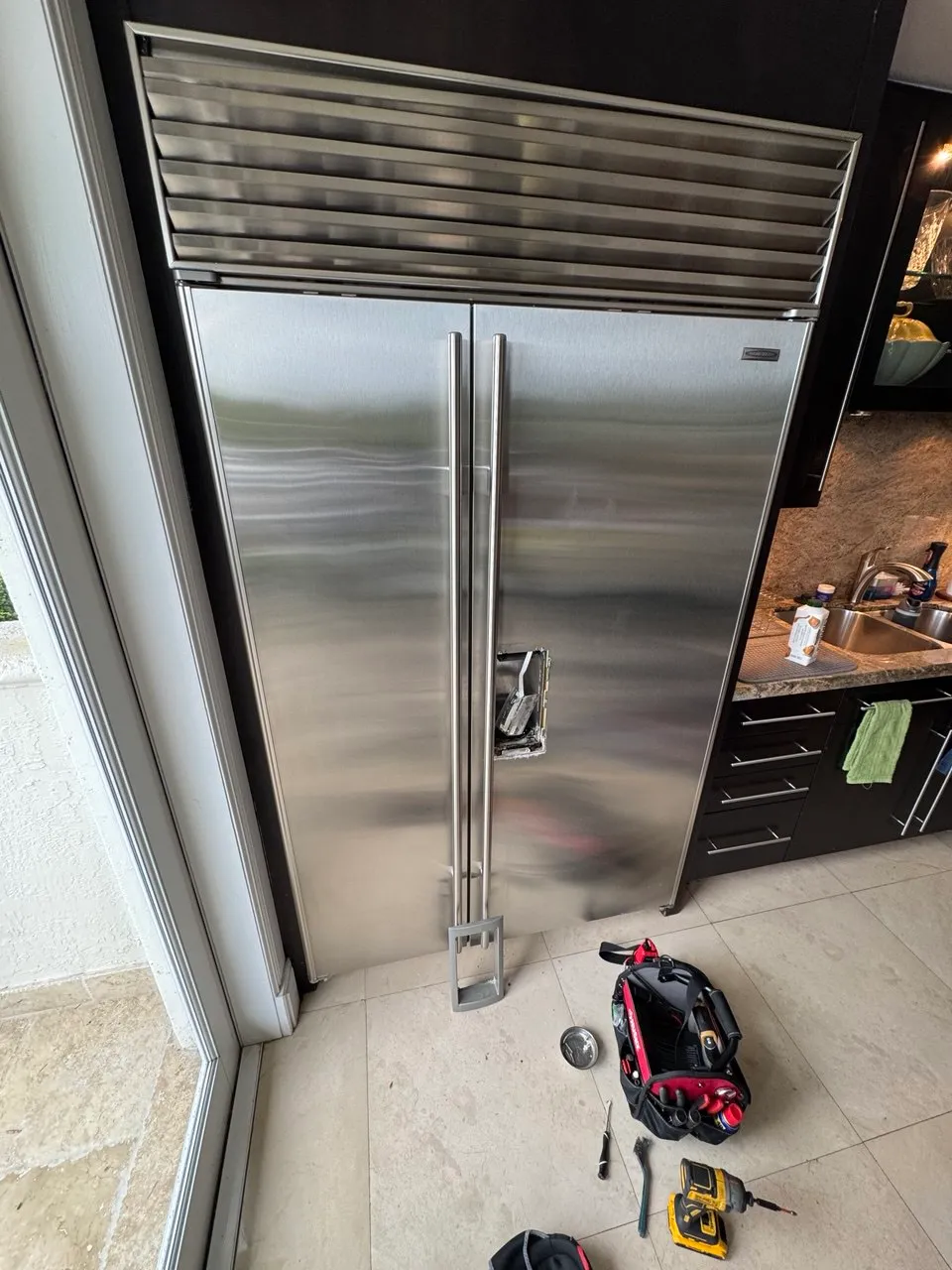Built-in Sub-Zero refrigerator with the dispenser panel removed and tools on the floor