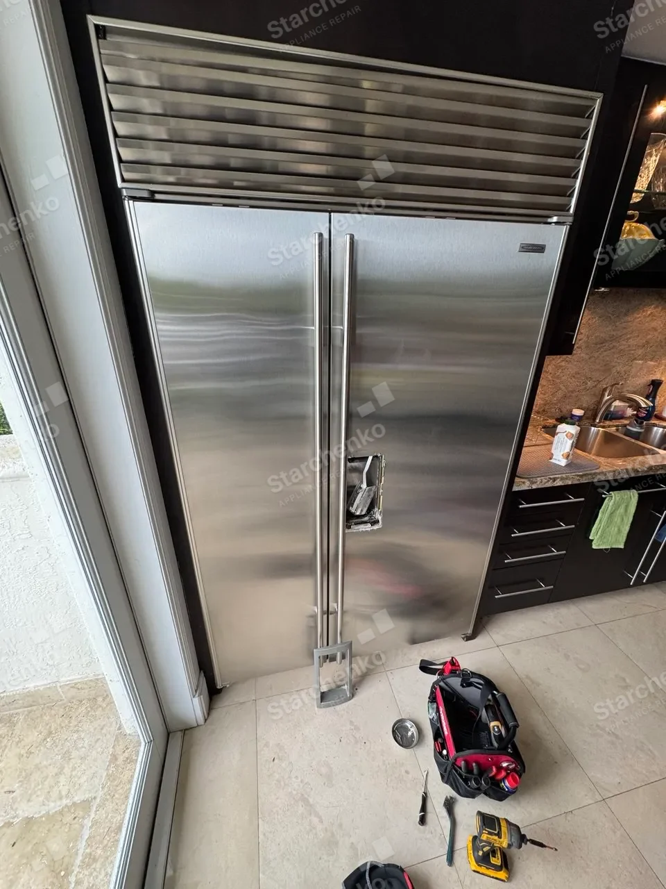 Sub-Zero built-in refrigerator with the dispenser panel removed and tools on the floor