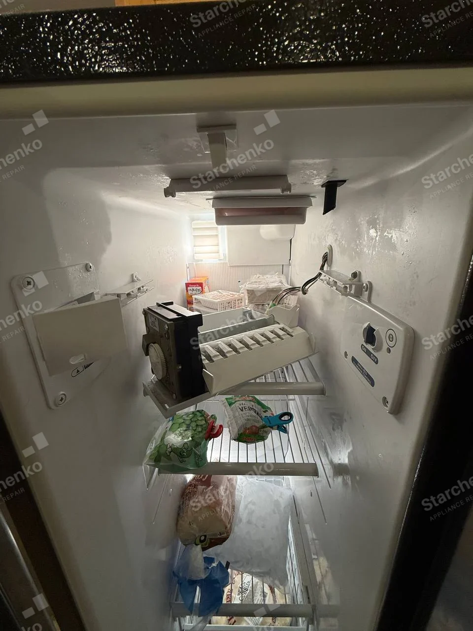 Samsung repair: Ice maker assembly pulled forward inside freezer compartment of household refrigerator, no appliance manufacturer mark.