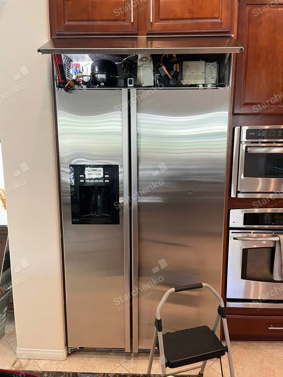 GE Profile repair: Profile logo visible at lower-left of refrigerator dispenser, top compressor compartment exposed.
