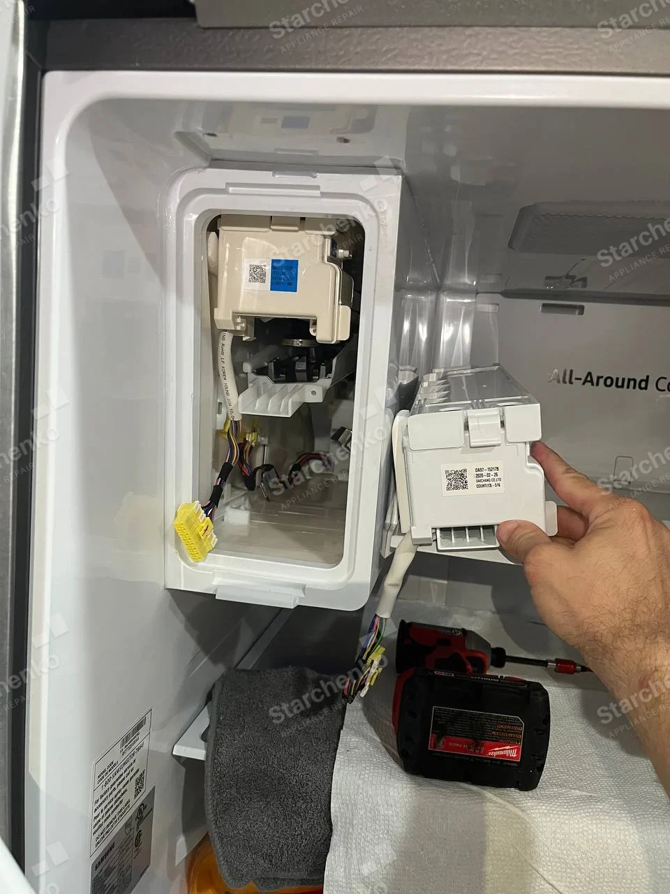 LG repair: Inside refrigerator fresh-food compartment, ice-maker housing open and removable assembly held beside it, All-Around Cooling text is feature label, not literal maker badge.