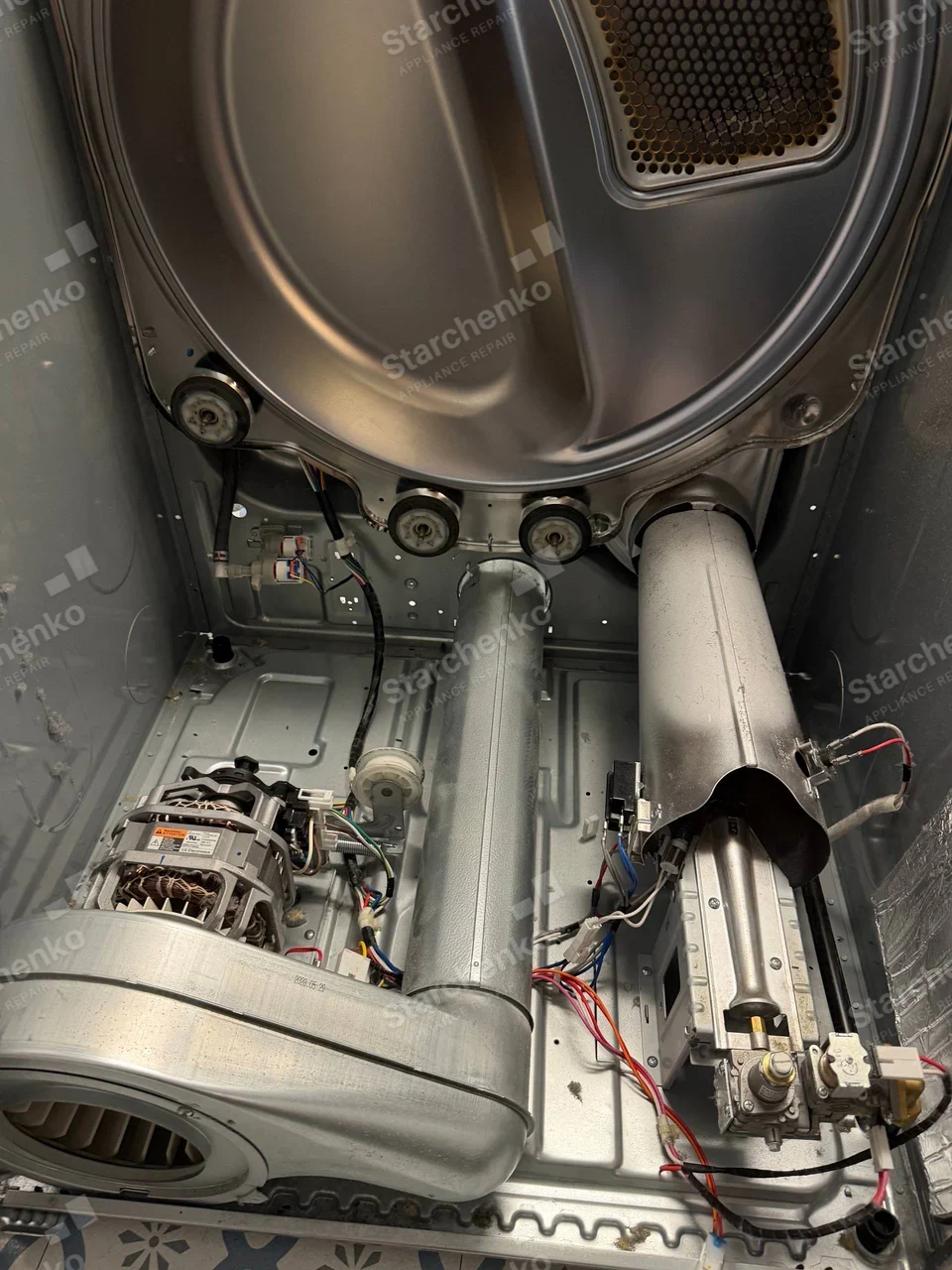 Samsung repair: Rear cabinet of gas dryer opened, exposing drum, blower, burner valve and exhaust duct.