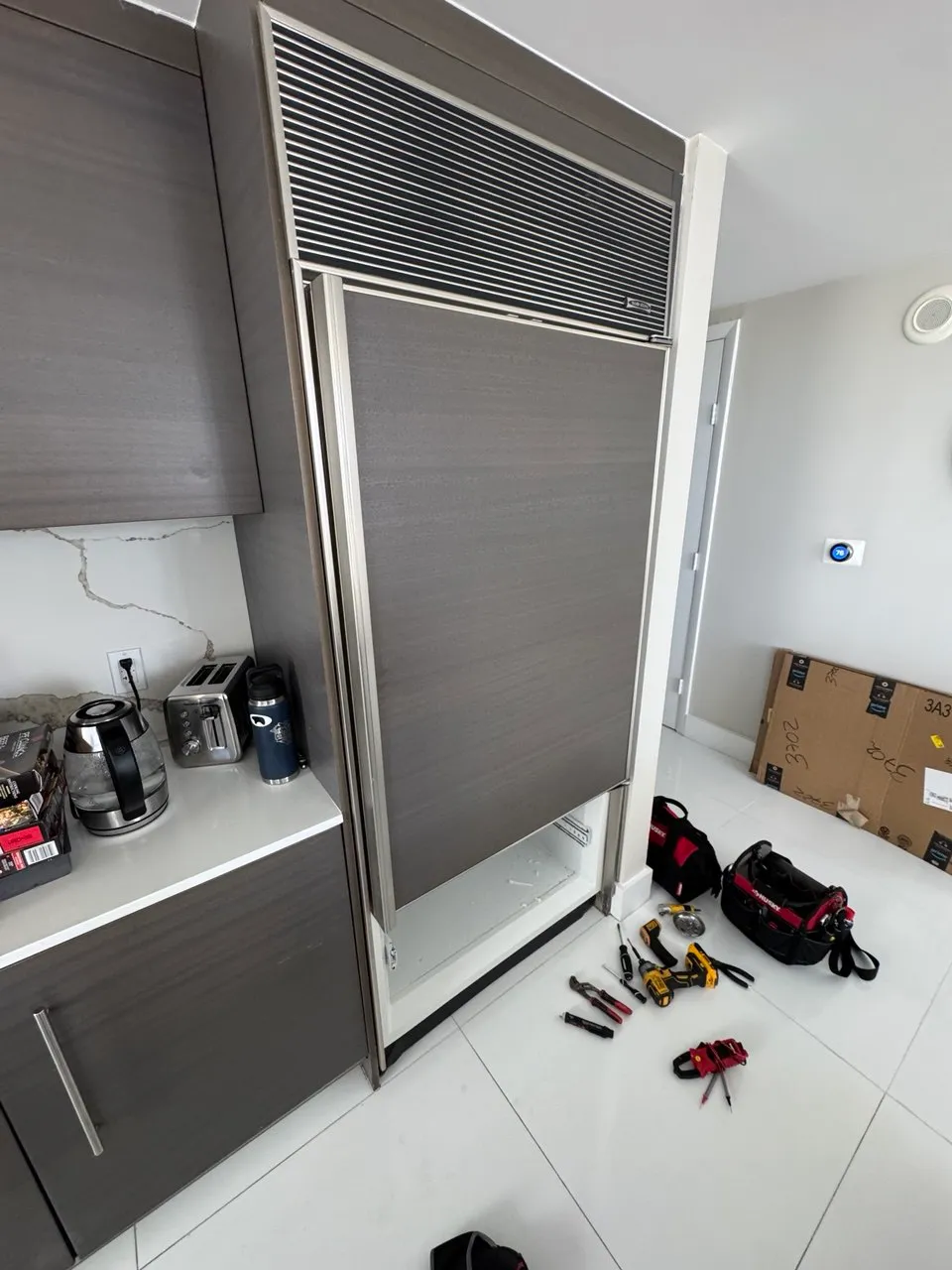 Panel-ready built-in refrigerator with the lower access panel removed and tools laid out