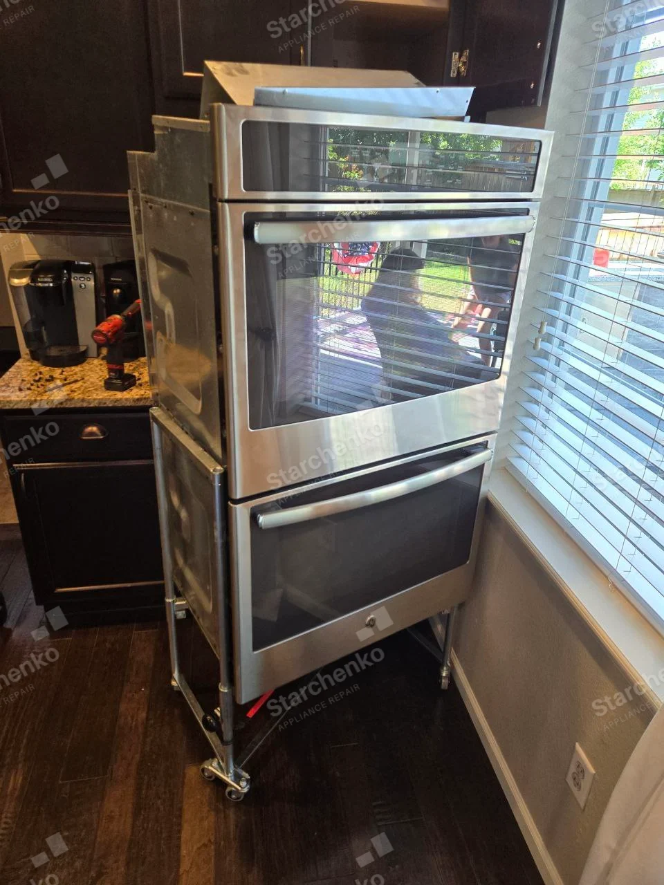 GE repair: Double wall oven pulled from cabinetry on service stand, side enclosure visible.