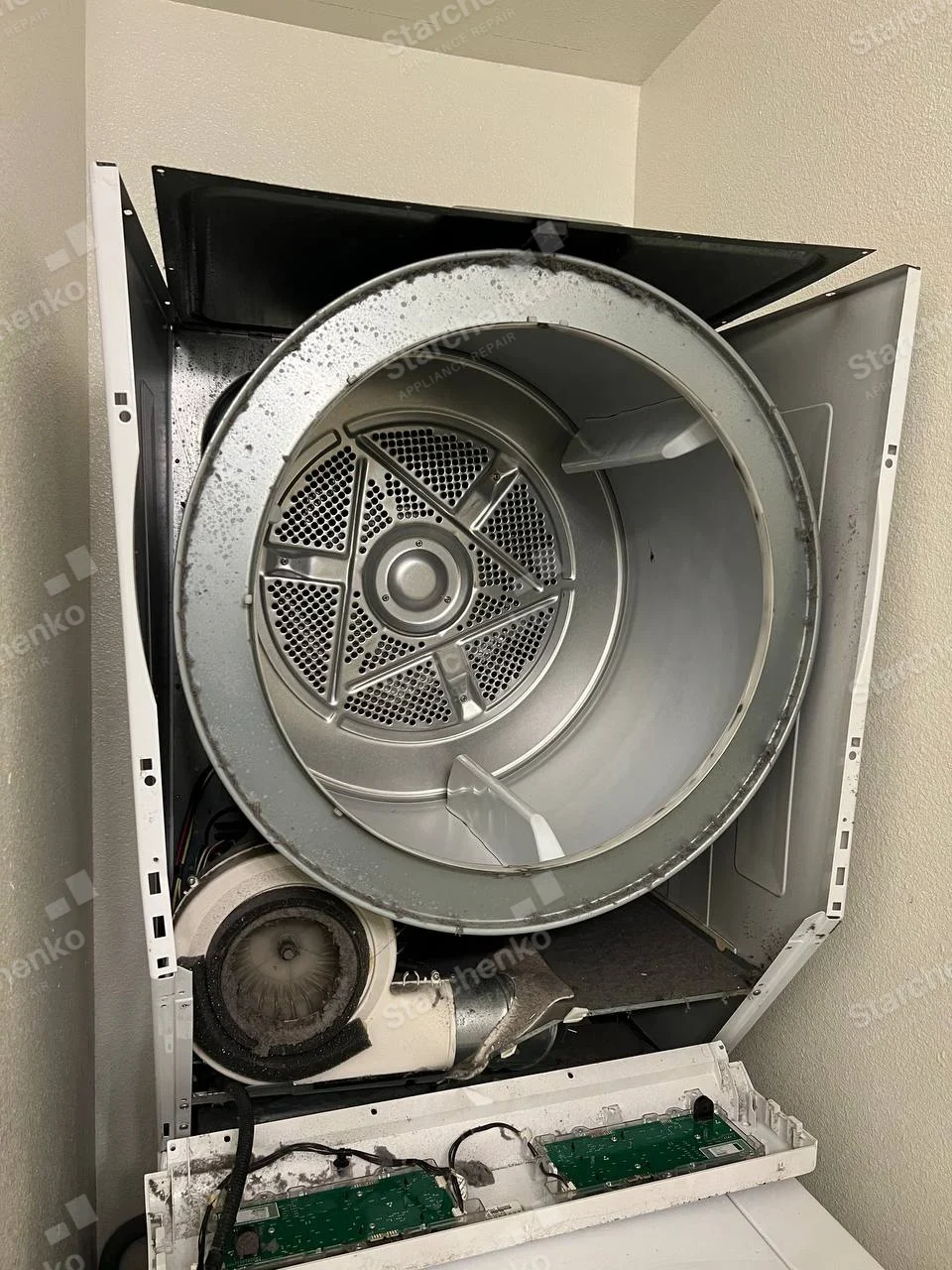 Whirlpool repair: Dryer front removed, exposing large drum, blower housing and detached control board.
