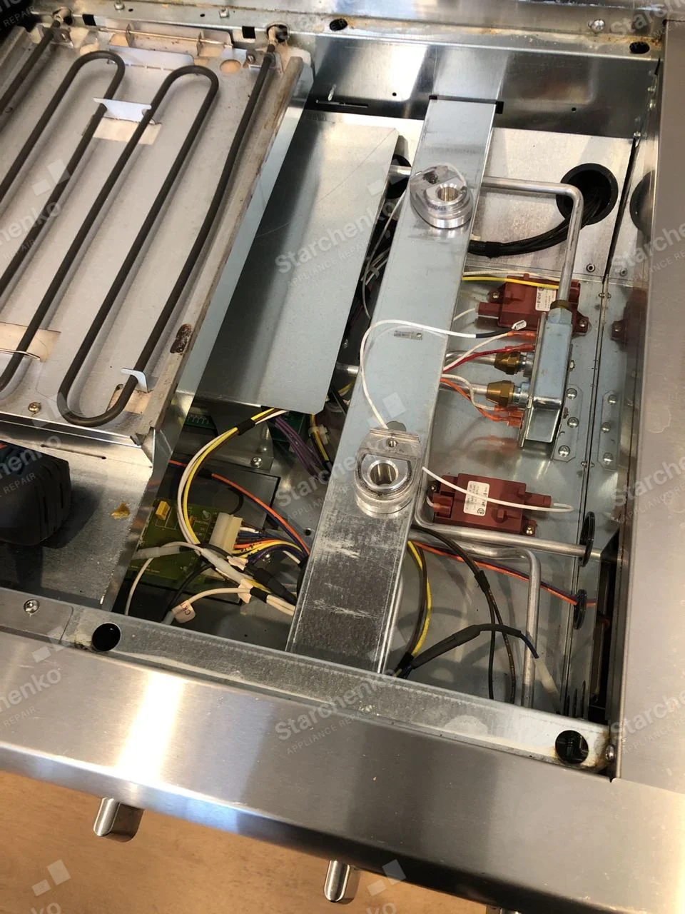 KitchenAid repair: Inside range cooktop with panel removed, showing heating element, gas lines and control wiring.