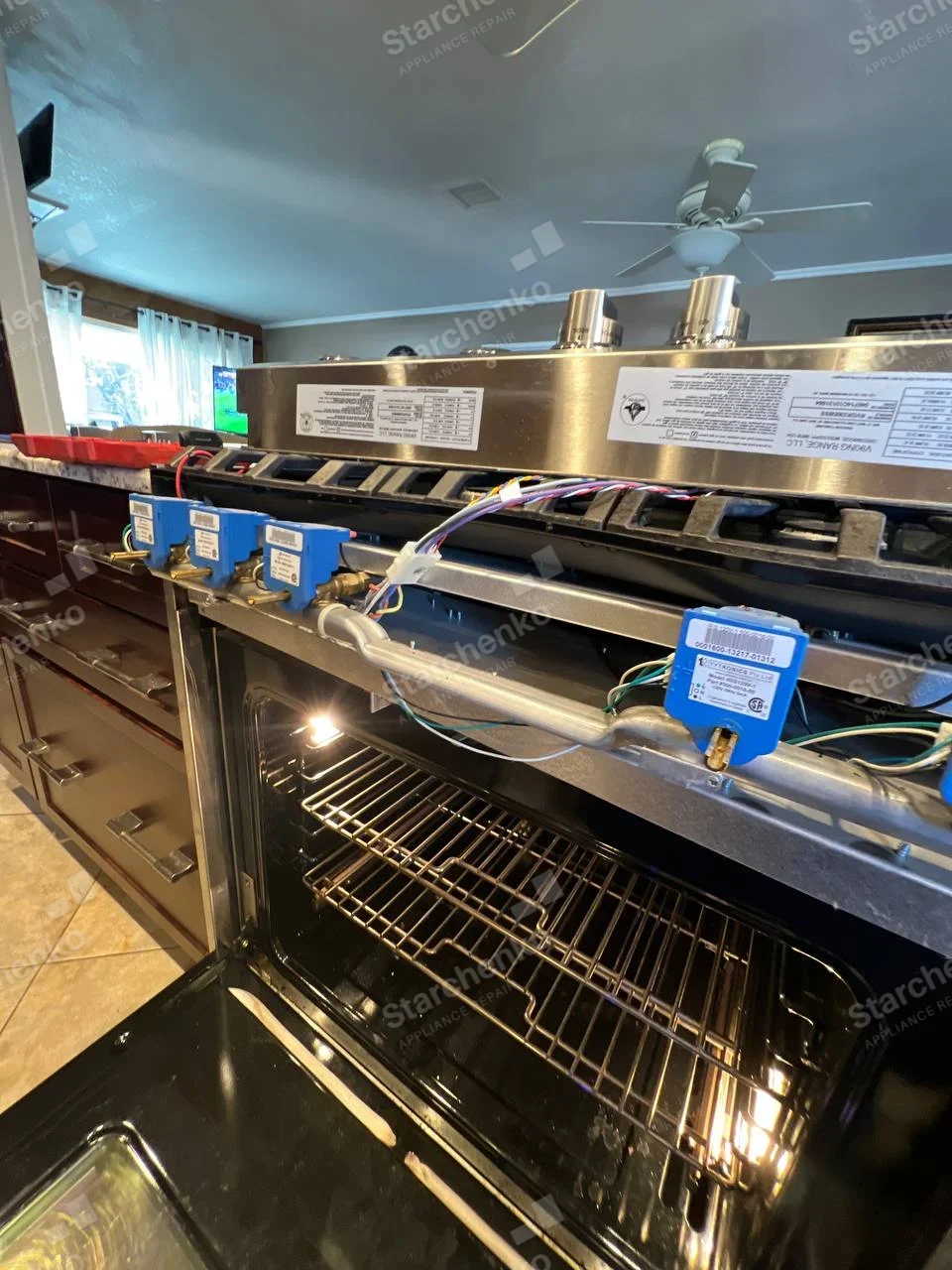 KitchenAid repair: Freestanding gas range with front control panel removed, exposing gas valves above open oven.