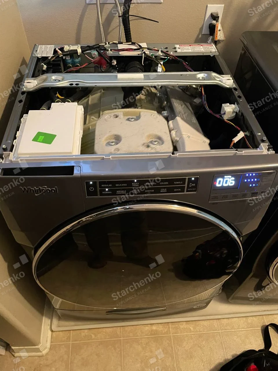 Whirlpool front-load washer with top cover removed, showing tub, dispenser and wiring.