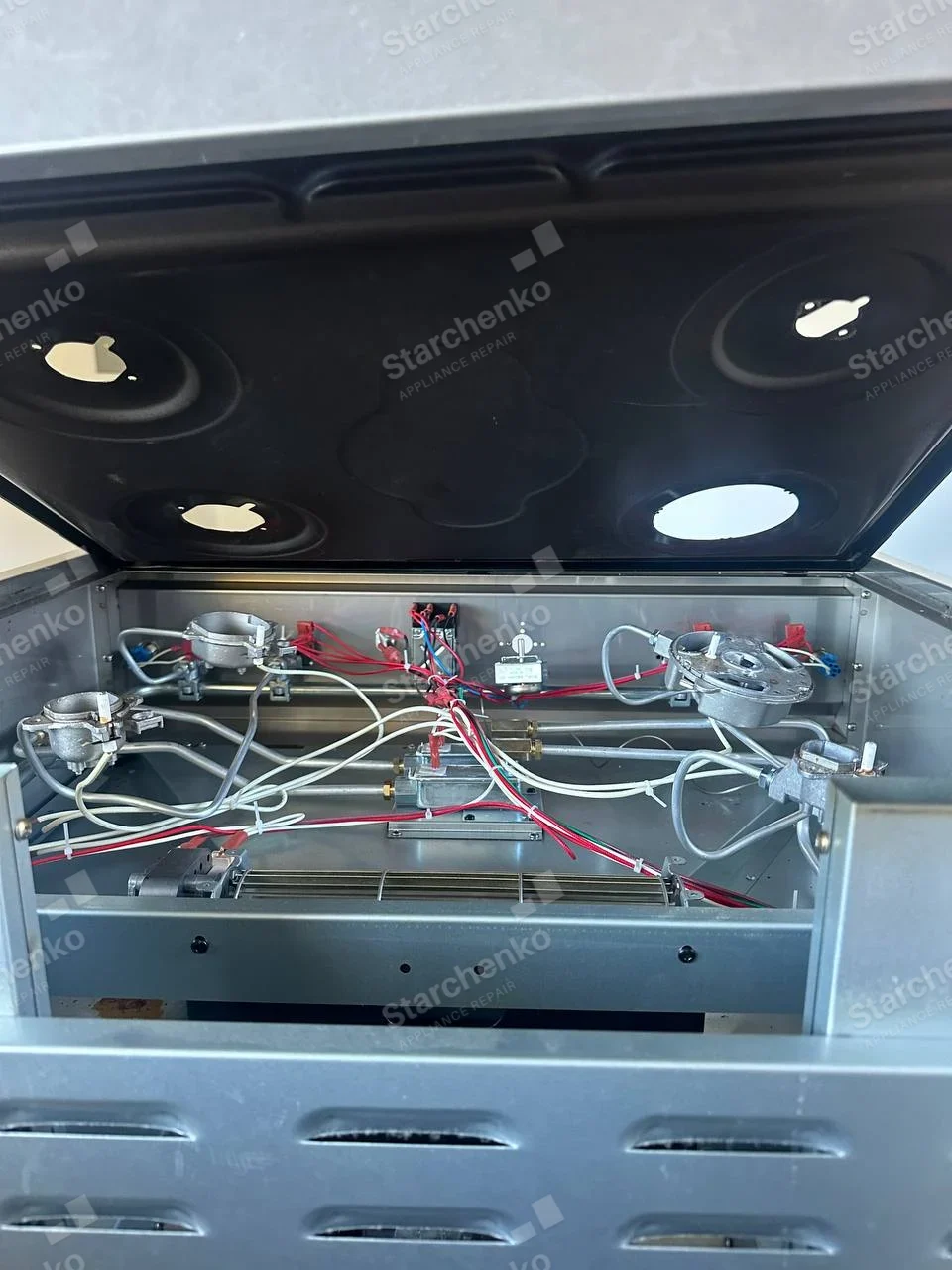 Whirlpool repair: Raised gas range cooktop showing burner bases, gas lines and ignition wiring.